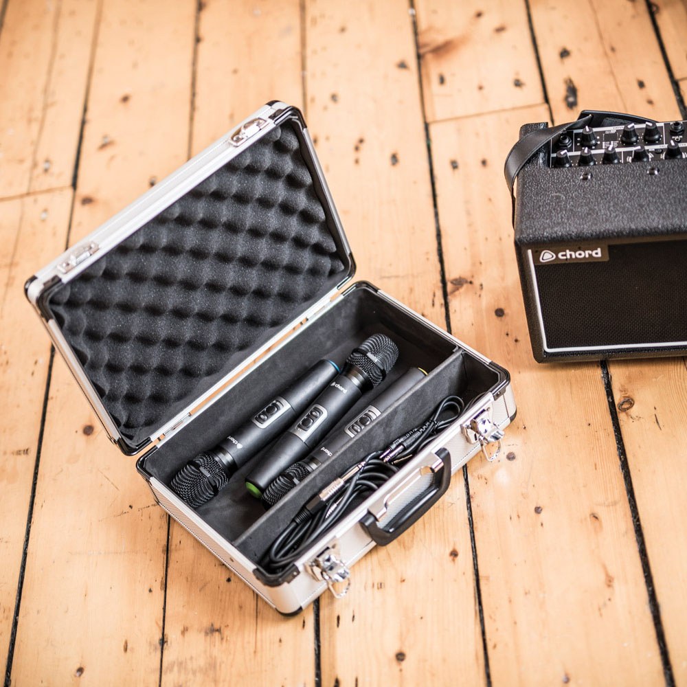 Chord MFC330 aluminium microphone flight case open on a wooden floor, showing three mics and cables inside foam padding beside a Chord amp.