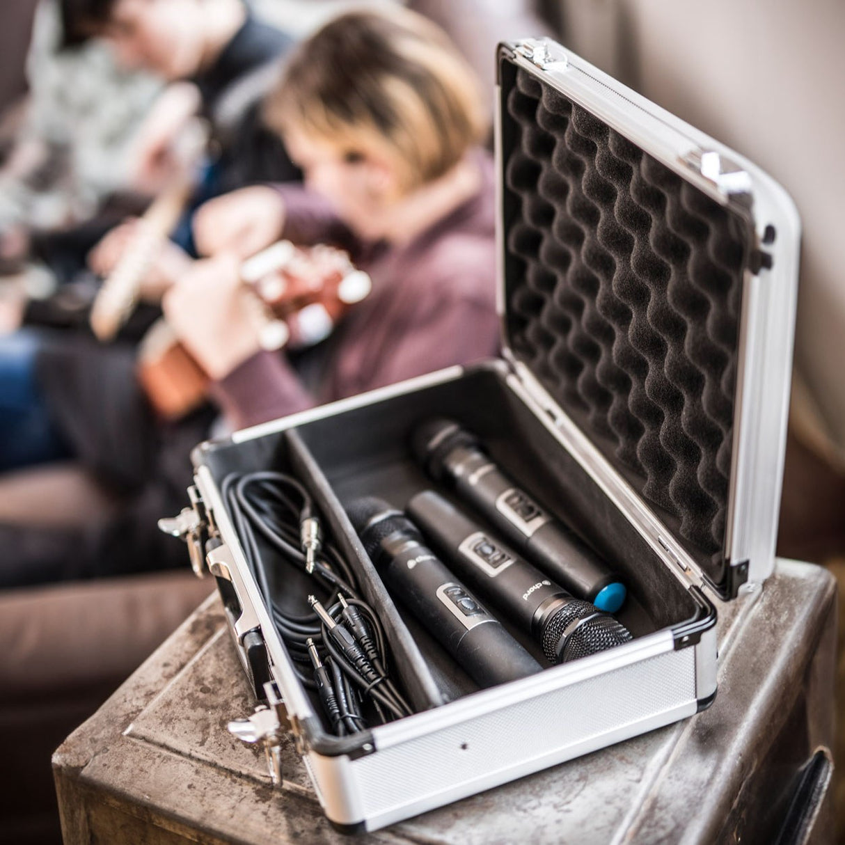 Chord MFC330 aluminium microphone flight case open on a crate, holding two wireless mics and coiled cables with a guitarist behind.