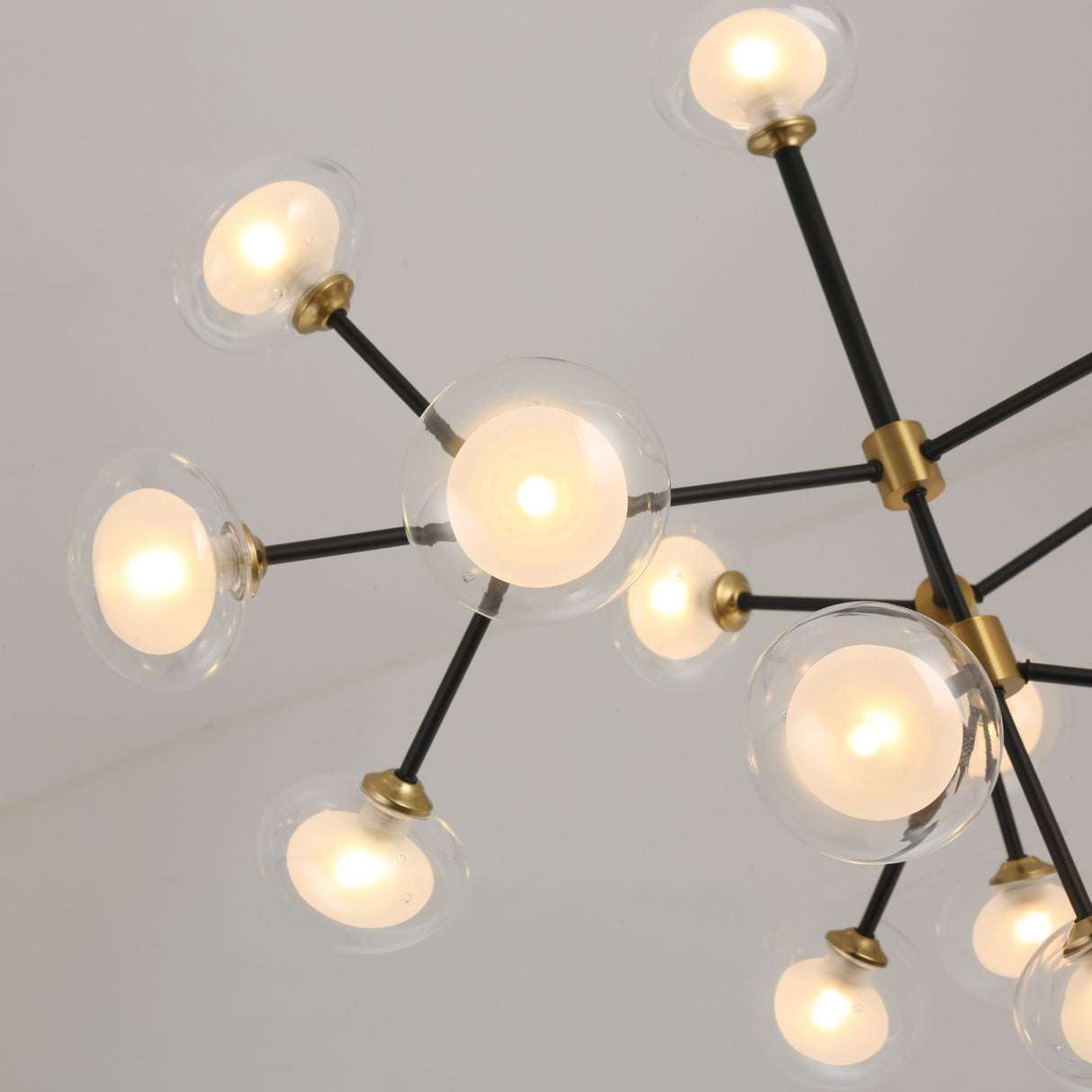 The Galaxy 12 Light Chandelier - Black & White features a modern starburst design with round glass globes and black metal arms, each globe housing a glowing bulb, shown from below against a white ceiling.
