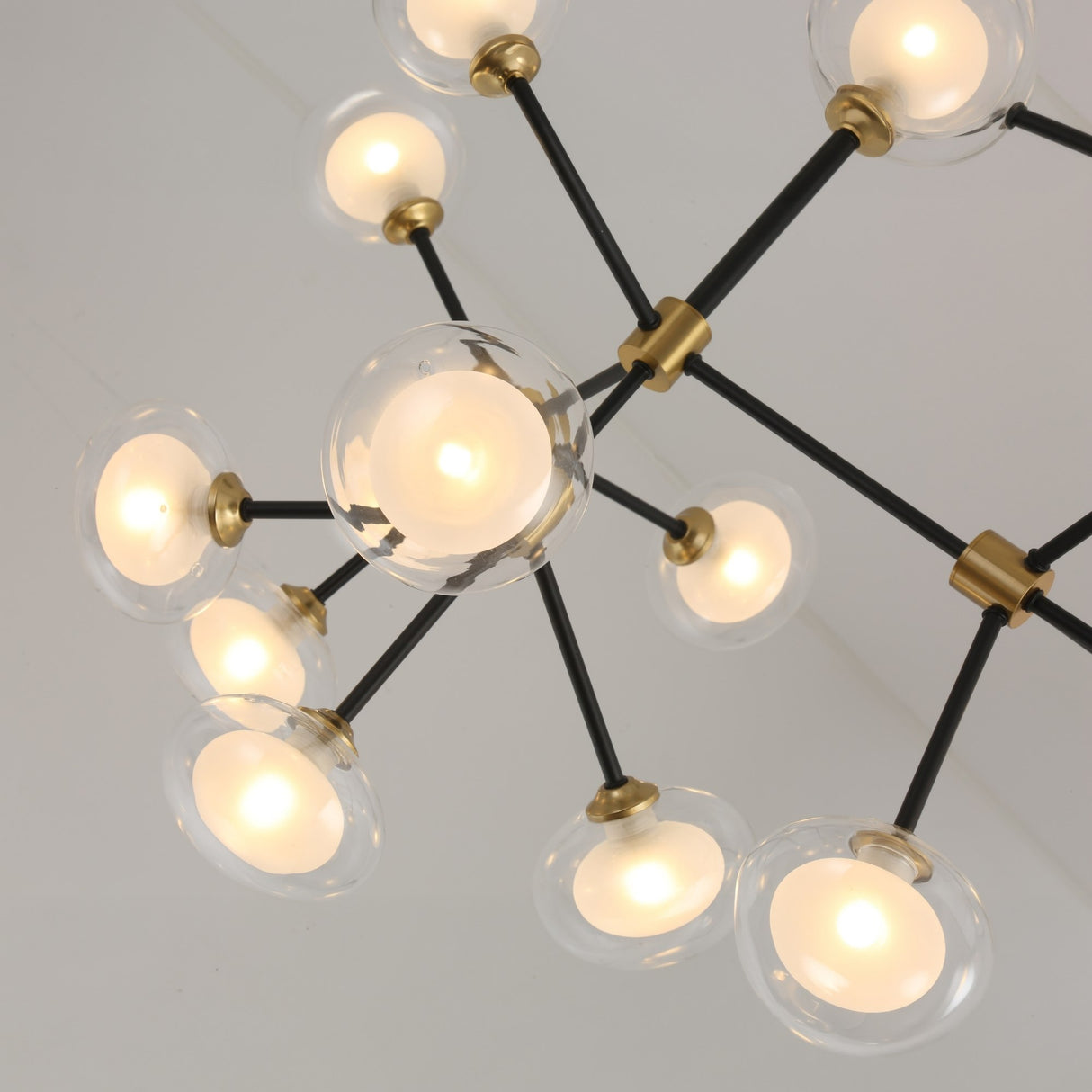 The Galaxy 12 Light Chandelier - Black & White showcases multiple round glass globes with glowing bulbs on black metal rods and brass accents, elegantly displayed against a white ceiling.