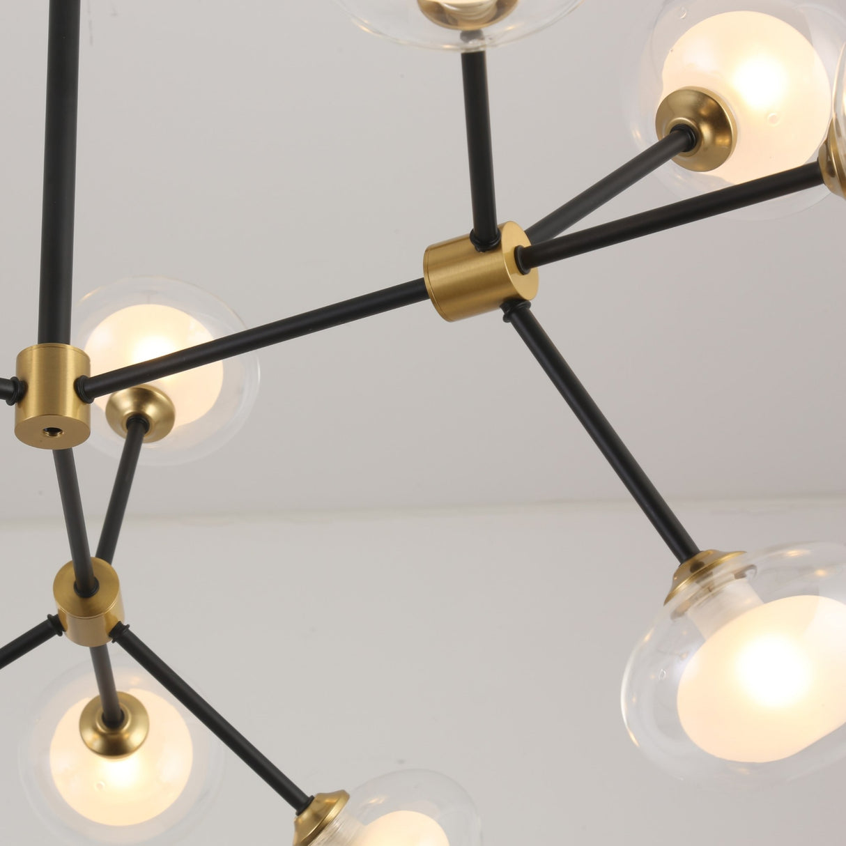 The Galaxy 16 Light Chandelier - Black & White showcases black rods, gold joints, and round glass bulbs in a bold geometric design, making a modern statement against a white ceiling.