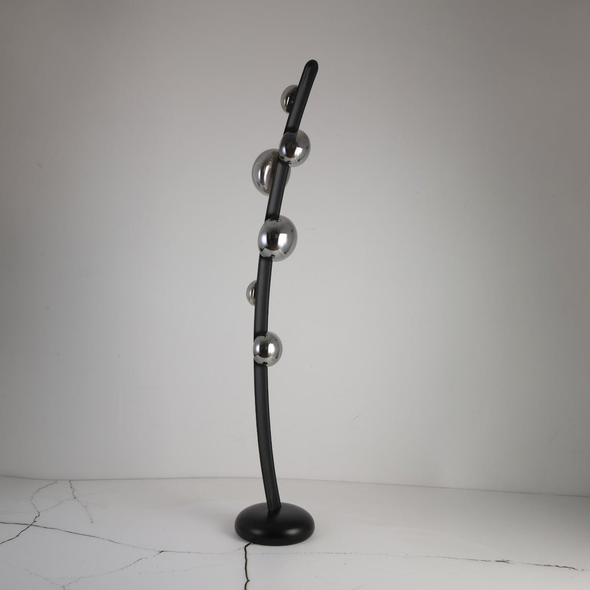 The Cordaro 6 Light Leather Floor Lamp - Black features a modern curved black rod with six metallic spheres, standing on a round black base placed on a cracked white surface.