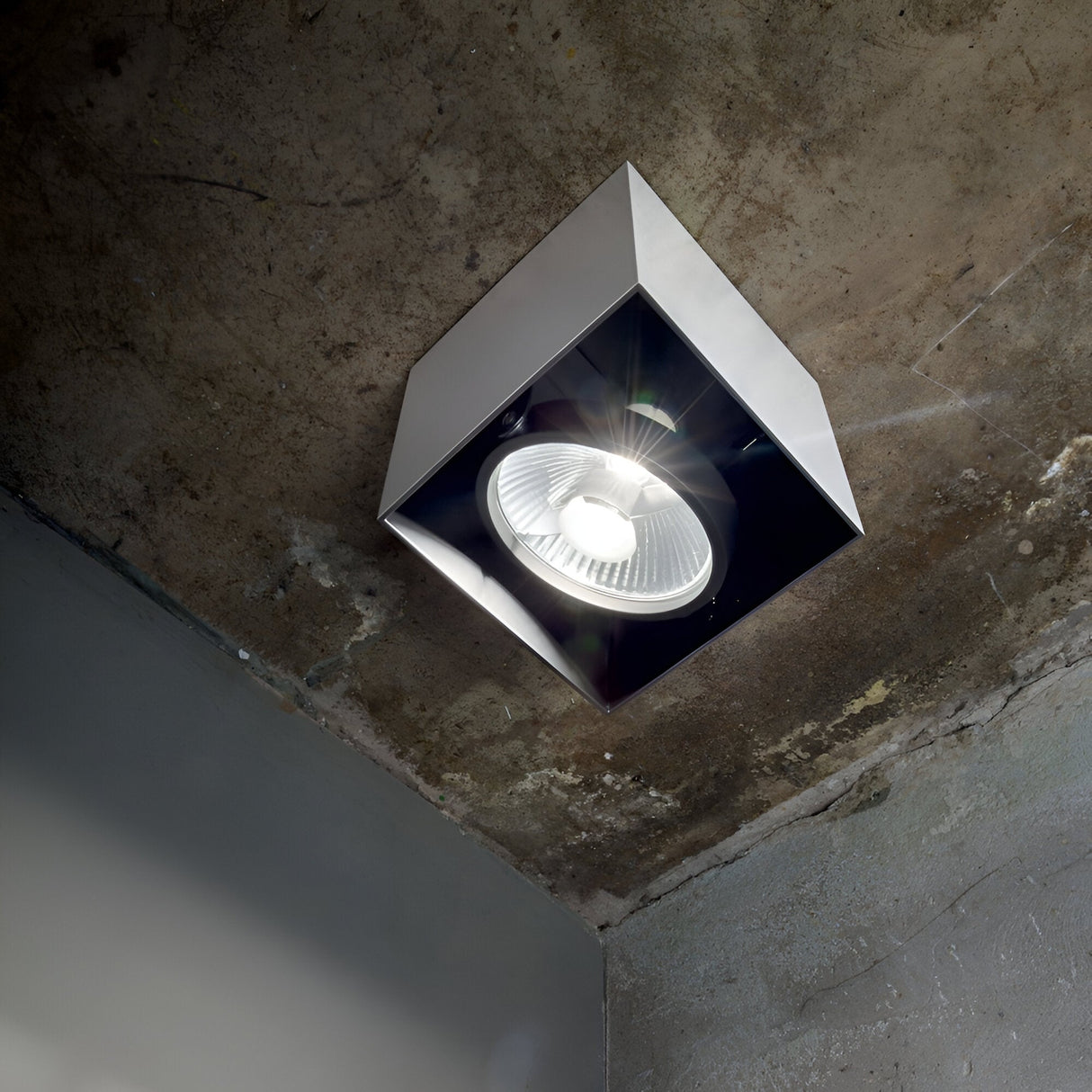 The Eclipsa Square Downlight - White, 15cm, is installed on a concrete ceiling. When illuminated, it emits a bright glow and offers a seamless look that beautifully contrasts with the industrial-style background, ideal for modern interiors.