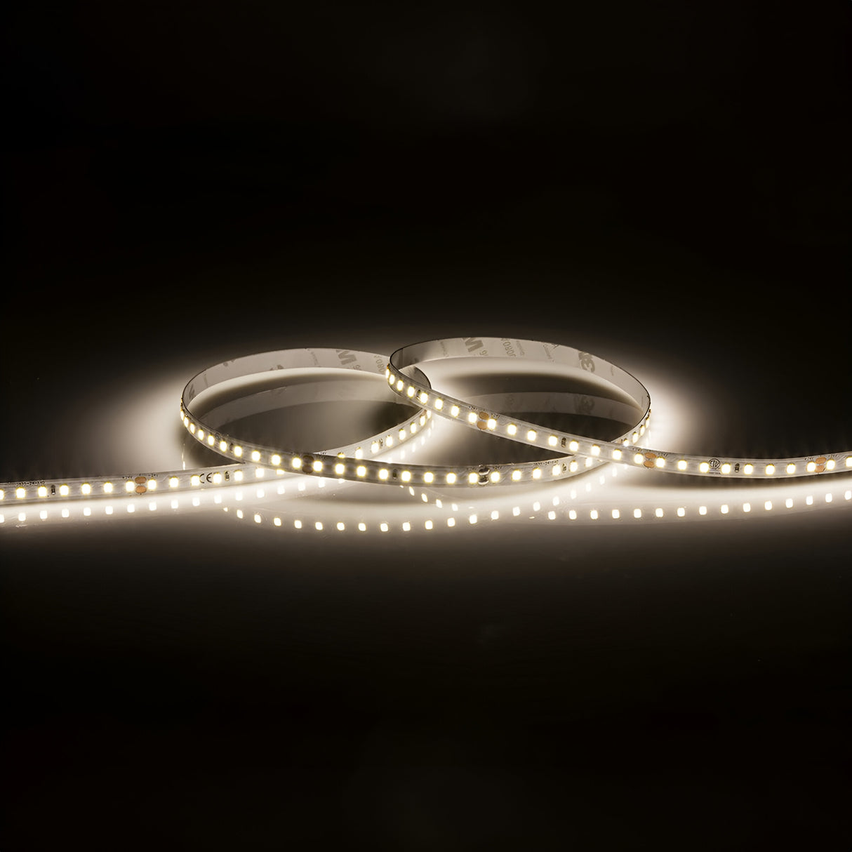 The 24V High Lumen LED Strip Light 4000K - 3m, set against a dark background, is loosely coiled to form two circular shapes. Its bright lights cast a warm and glowing effect on the surrounding area.