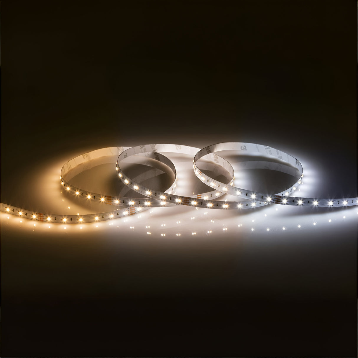 Three loops of the 24V CCT LED Strip Light 2700K to 6000K - 3m are arranged, with one strip emitting a warm yellow light, the second providing ambient lighting in medium white tones, and the last producing a cool bright white glow, all set against a dark background.