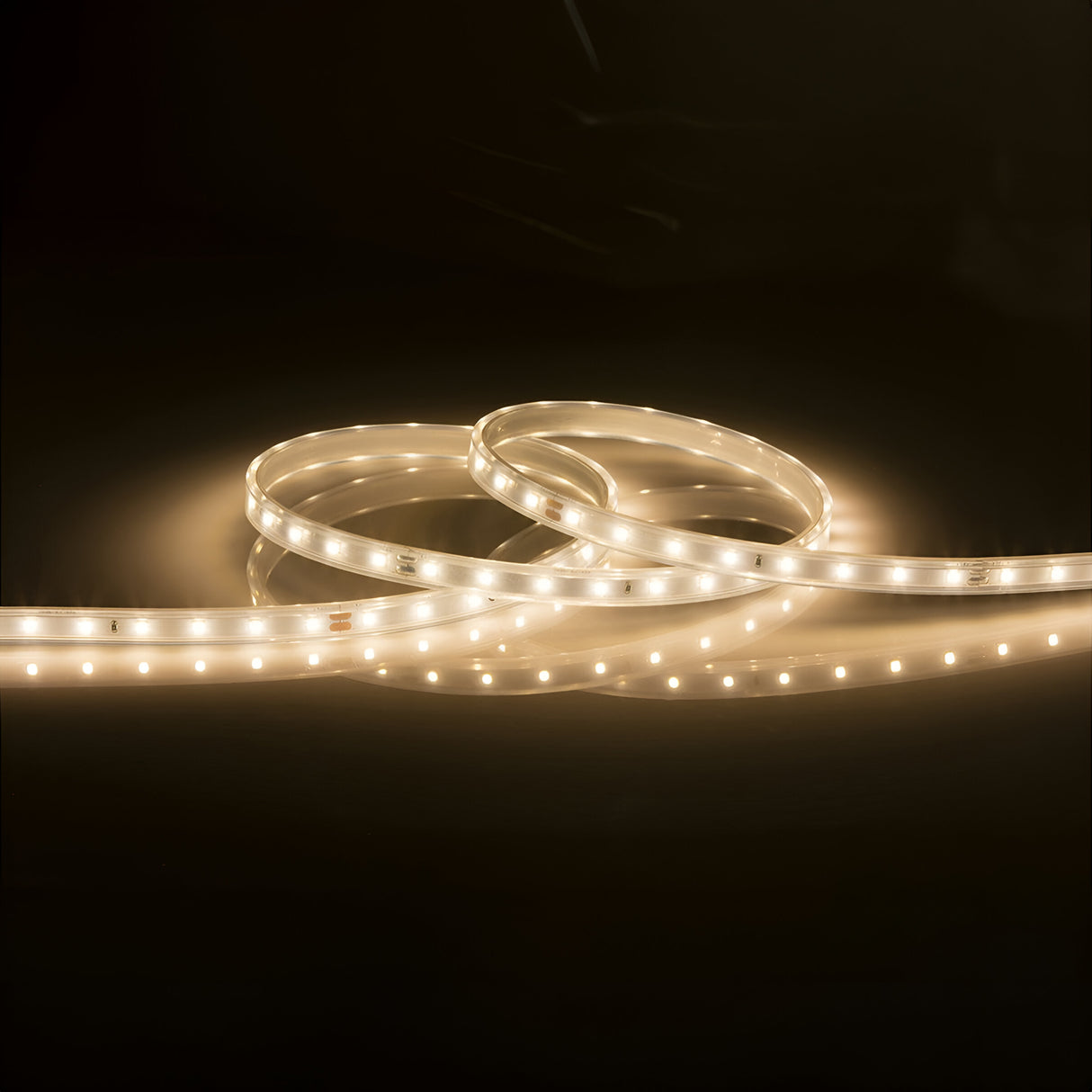 A 24V LED Strip Light IP67 3000K - 5m emits a warm white glow against a dark background. The evenly spaced lights form a continuous line of illumination, subtly reflecting on the surface below while providing IP67 protection for versatile installations.