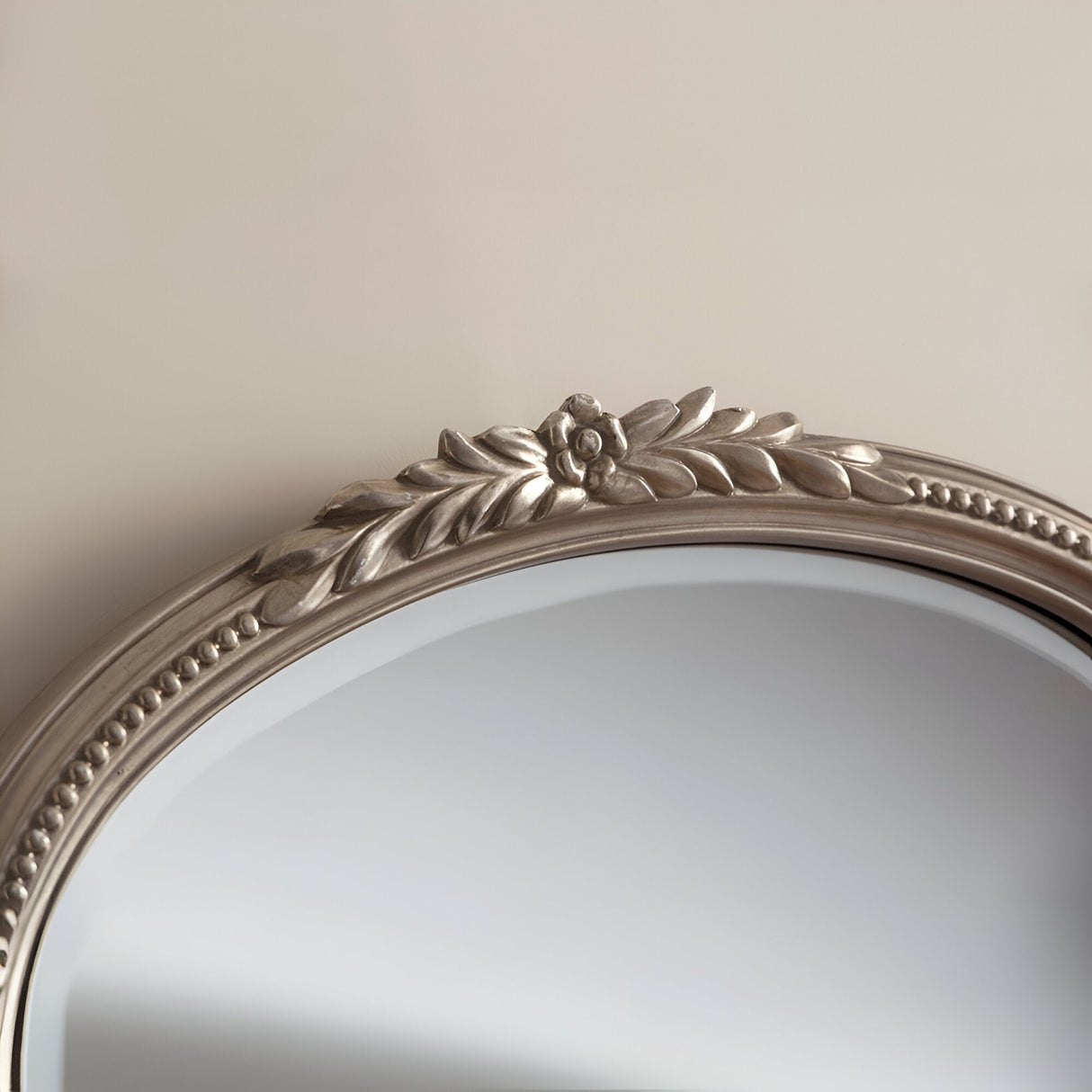 A close-up of the Mist Arched Wall Mirror Silver - 94x63cm showcases its decorative floral design. The metallic frame, with its sophisticated silver finish, features an intricately carved flower and leaf pattern set against a neutral background. The mirror itself is partially visible.
