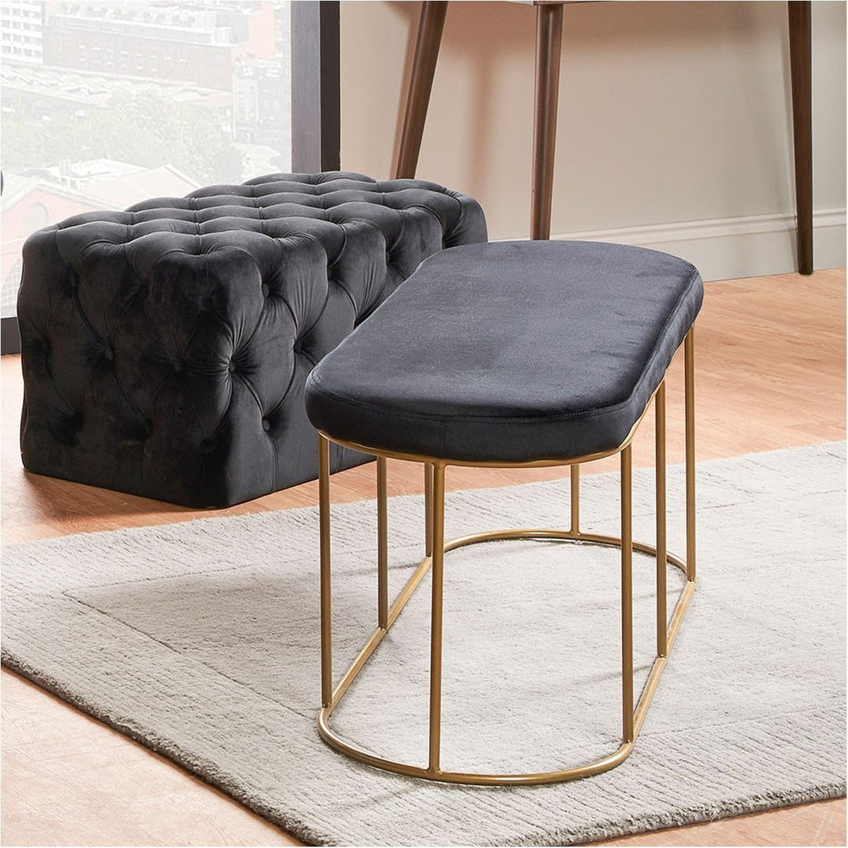 Nino Black Velvet & Gold Iron Bench, oval padded seat on an open gold iron frame, shown beside a matching tufted black storage ottoman in a living room setting.