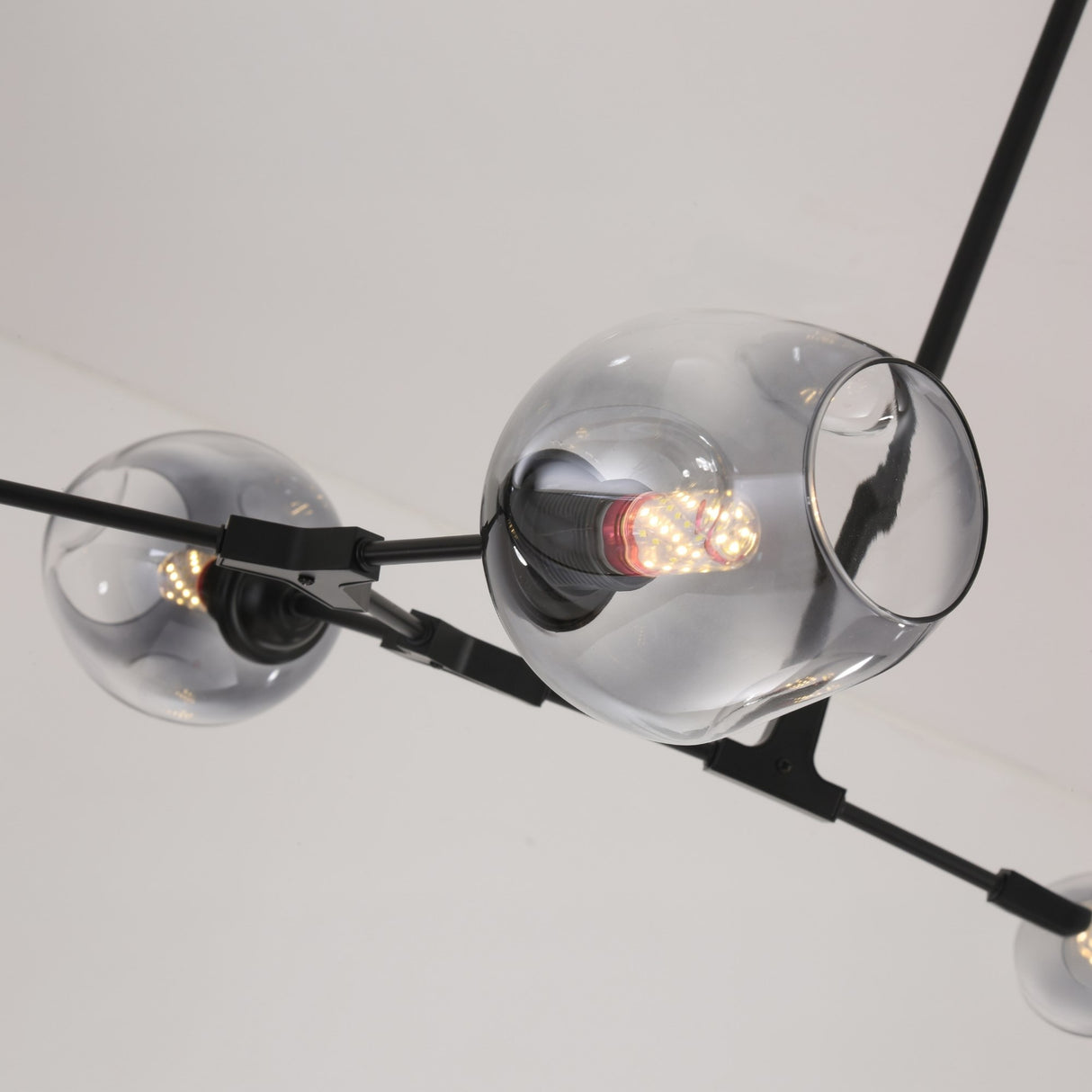 Close-up of Niori Tree 8 Light Branching Suspension showing smoked glass globes with lit E27 filament bulbs on matt black arms against a white ceiling.