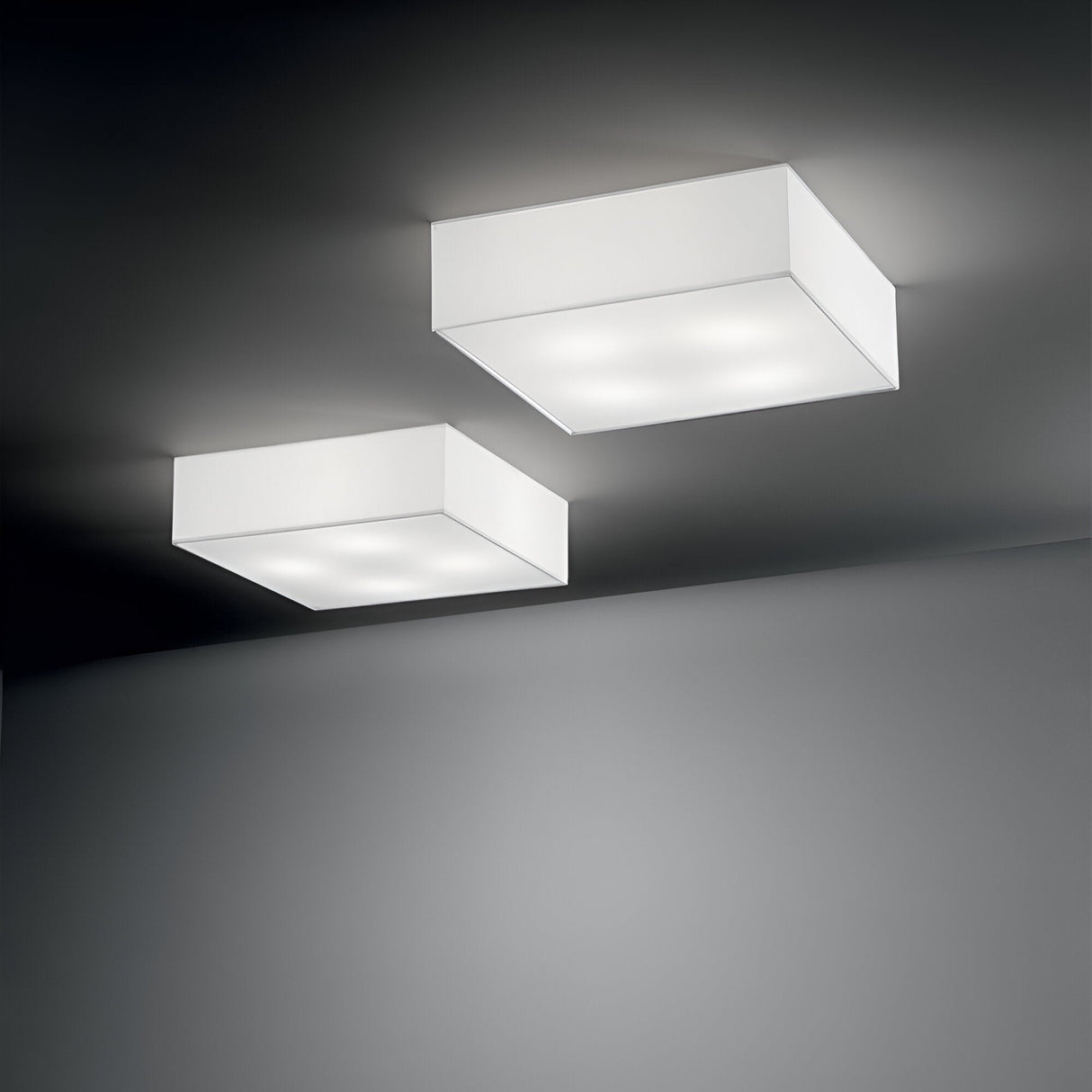 Two Dream 4 Light Flush fixtures, each measuring 40cm and featuring a white finish, are mounted on a gray ceiling. They cast a soft, diffused glow that enhances the modern aesthetics of the space with their clean lines and minimalist design, offering a compact lighting solution.