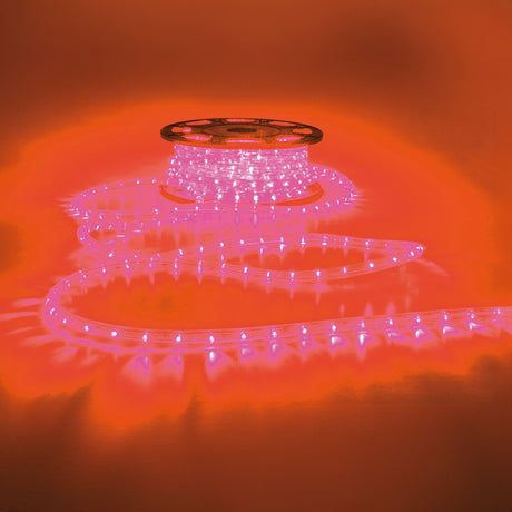 A spool of LYYT 230V IP44 LED Rope Light in red is coiled on a reflective orange surface, casting a vibrant glow and ambiance in the surroundings. Its flexible tube allows for versatile placement, enhancing visual appeal with its weather-resistant design.