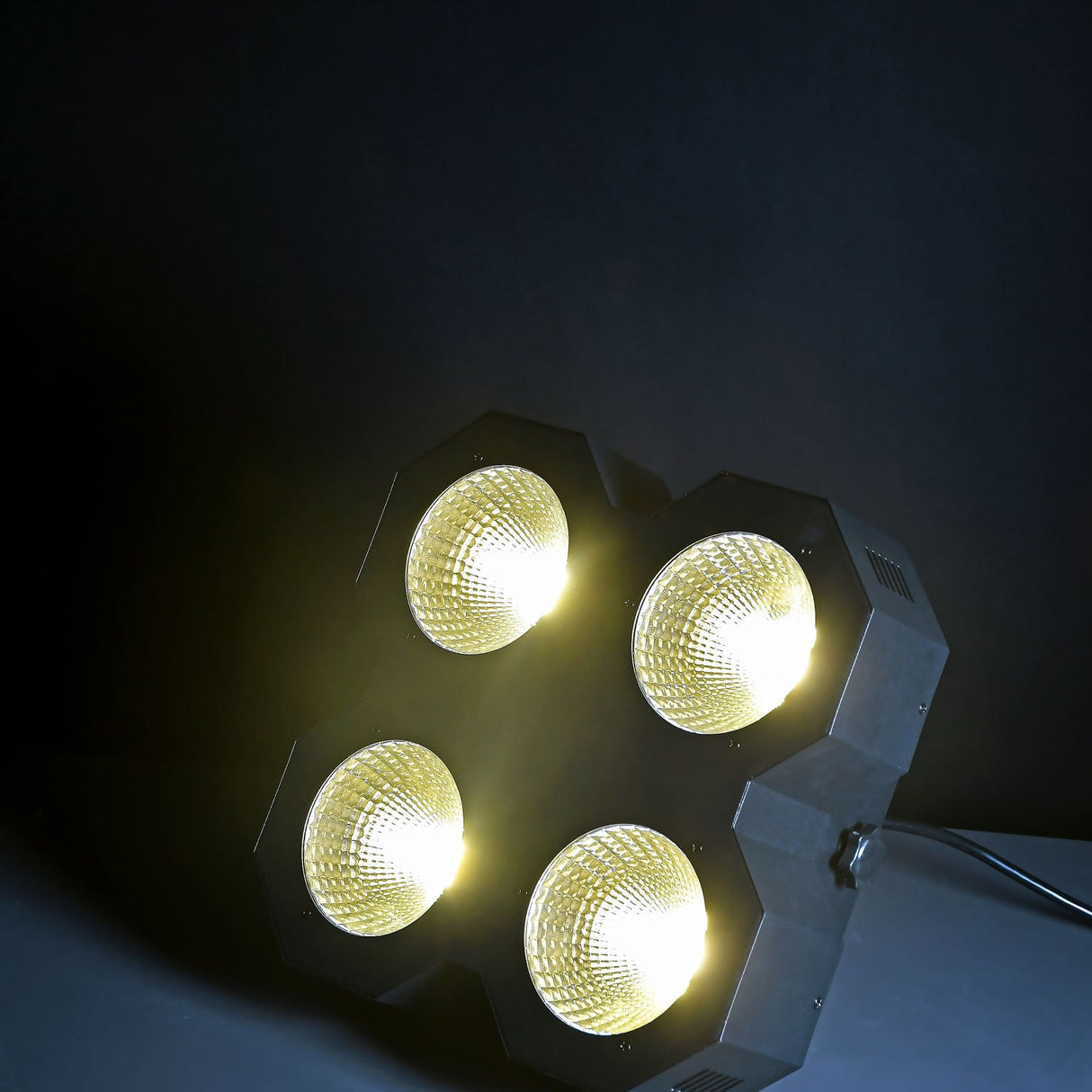 QTX 4x50W LED wash light by AVSL illuminated in warm white, showing four COB lenses in a square metal housing against a dark background.