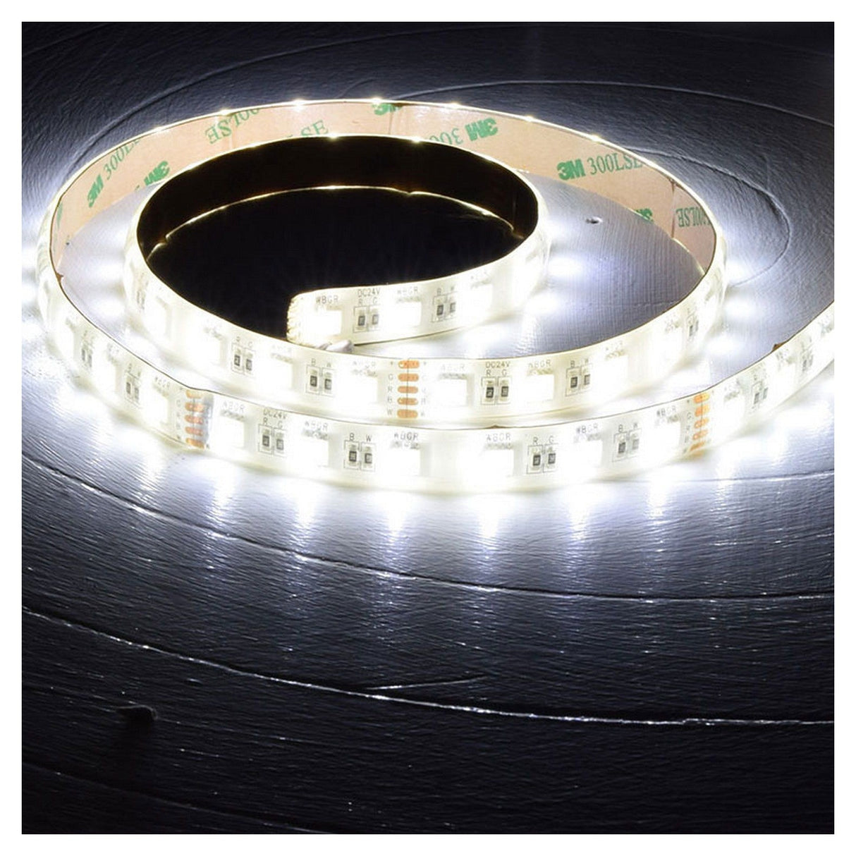 The LYYT 24V RGBW LED Strip Light 5m - 60 LED/m emits a bright glow on a dark surface. This thin, flexible strip, equipped with a self-adhesive backing, features small lights evenly spaced along its length, beautifully illuminating the surrounding area.