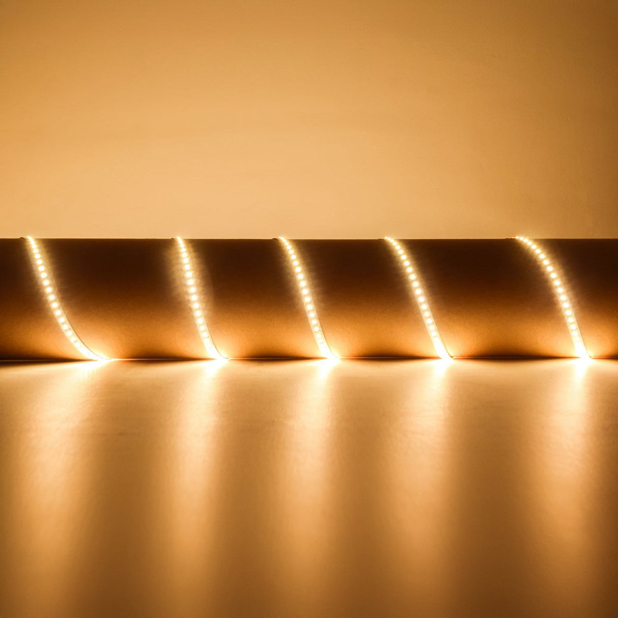 A golden spiral of light coils along a smooth surface, casting a warm glow with its high luminous flux output. The LYYT 24V High Output LED Strip Light - 3000K creates bright parallel lines that enhance the area's luminous and reflective qualities effortlessly, thanks to its convenient self-adhesive backing.