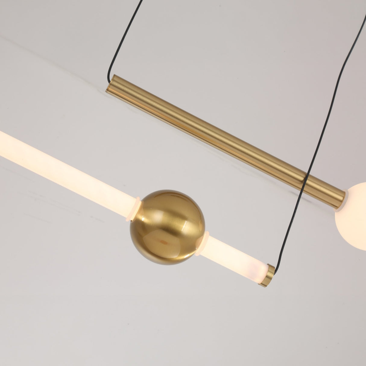 The Sottile LED Horizontal Suspension Light - Gold features a minimalist design with a gold cylindrical bar, central gold sphere, and two glowing white tubes gracefully suspended by thin black wires.