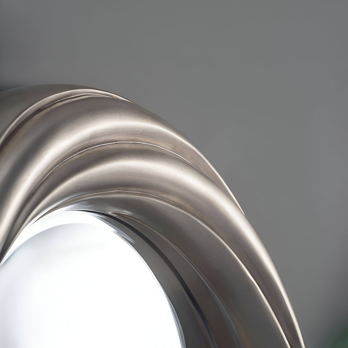 Close-up of the Iris Circle Wall Mirror Silver - 84cm, showcasing its silver metallic frame with curved, smooth ridges against a gray background, reflecting light with modern elegance.