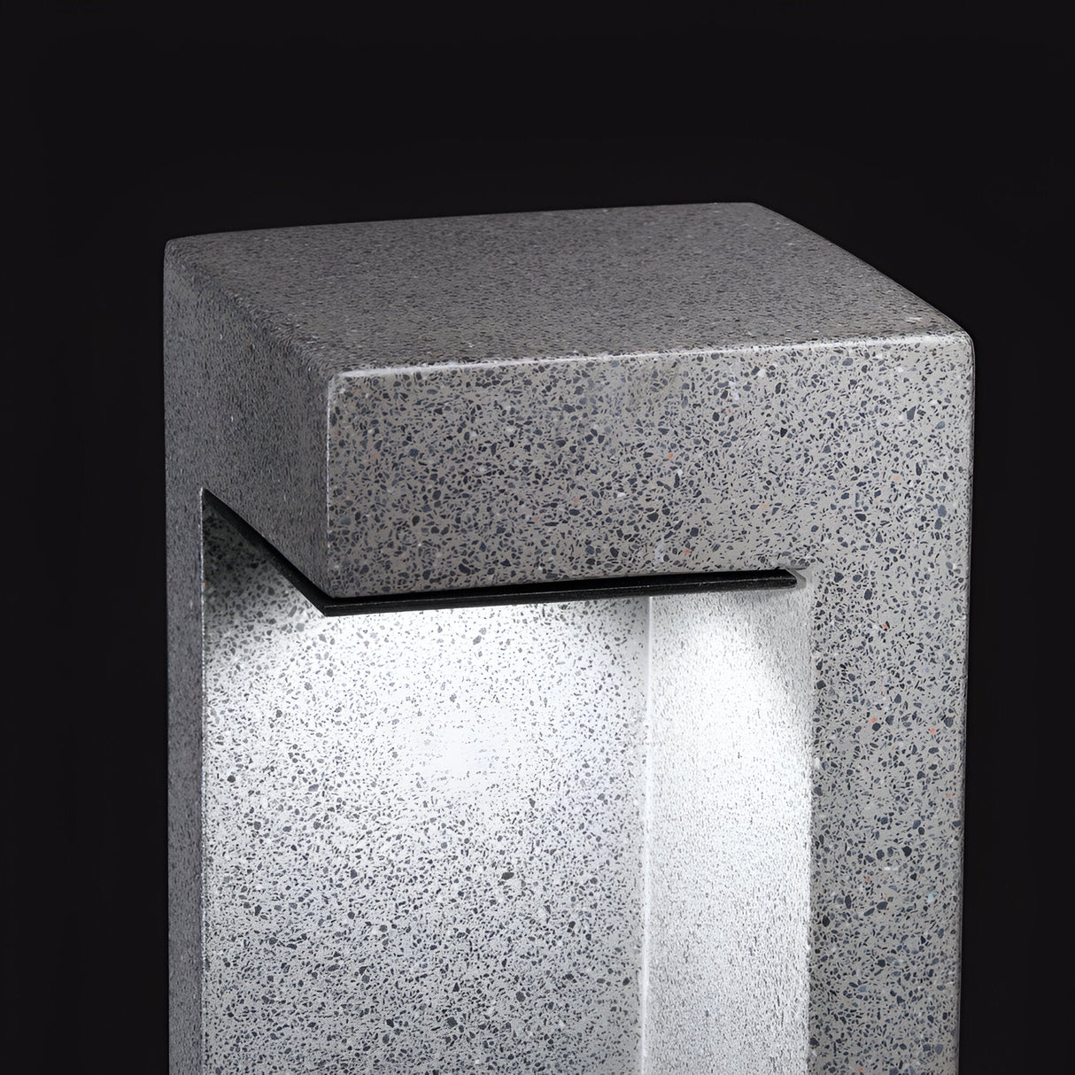 The Starry Outdoor LED Bollard Light 9W 4000K in grey boasts a modern, rectangular concrete design that emits a soft white light. Featuring minimalist aesthetics and an open central space, it showcases smooth, speckled surfaces set against a black backdrop. Engineered for energy-efficient performance, this LED bollard combines style with outdoor durability at a height of 49cm.