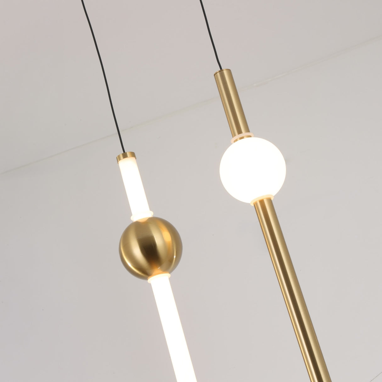 Two Sottile LED Vertical Suspension Lights in gold with round white bulbs hang from the ceiling, highlighting their modern minimalist design against a plain white background.