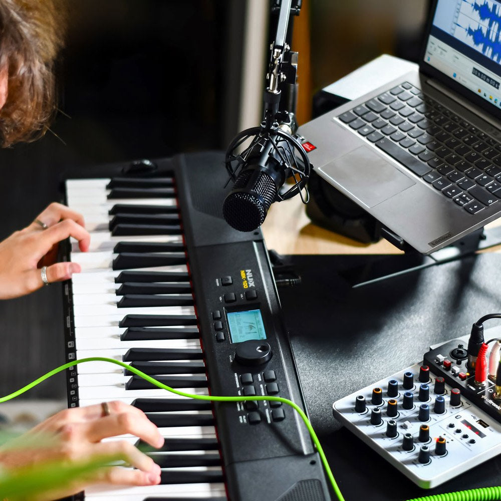 Citronic Q-PAD compact mixer by AVSL on a studio desk beside a keyboard, microphone and laptop, with rotary controls and green cable connected.