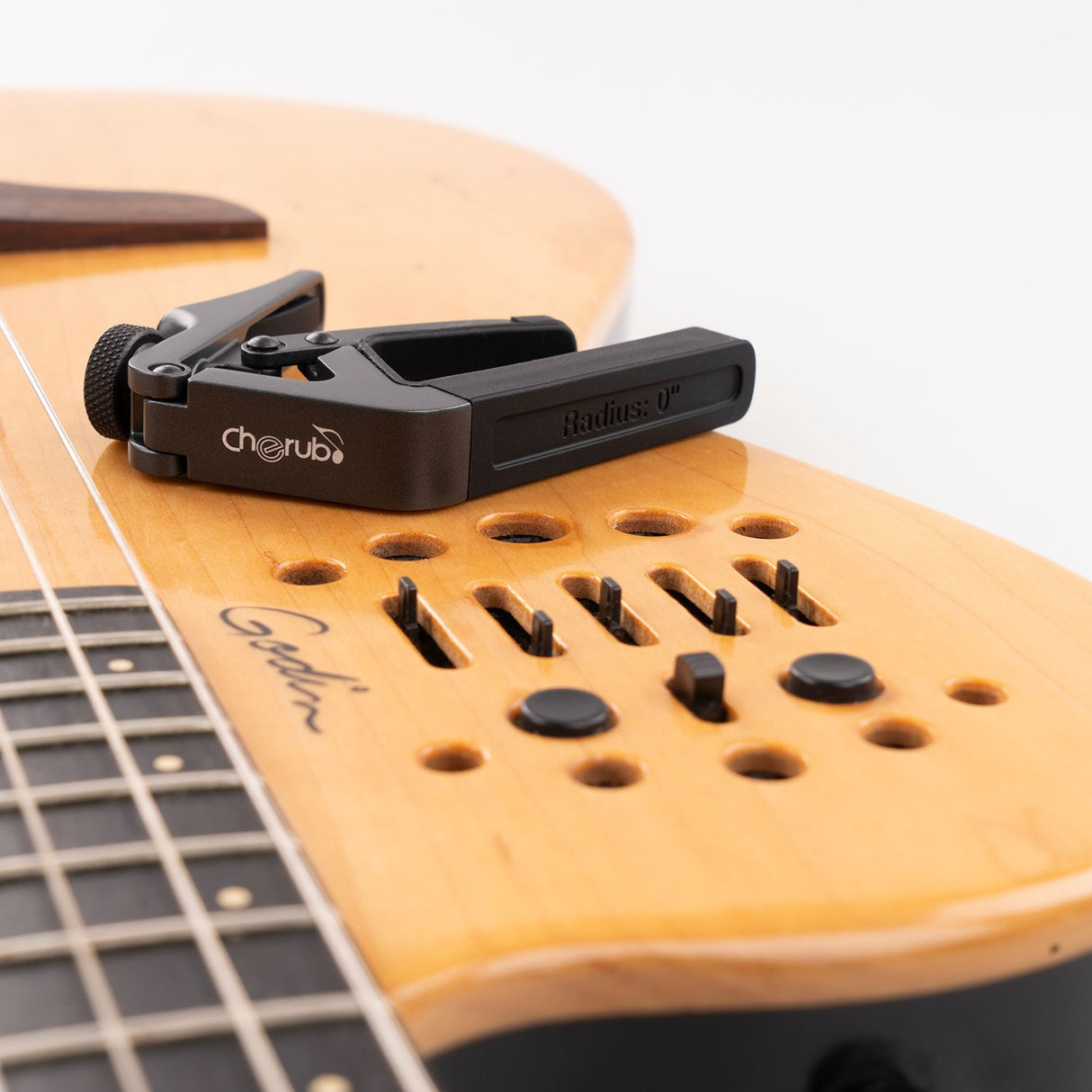 Cherub CGC-1 Gemini adjustable guitar capo in matte black resting on a natural wood Godin guitar body with visible control buttons.