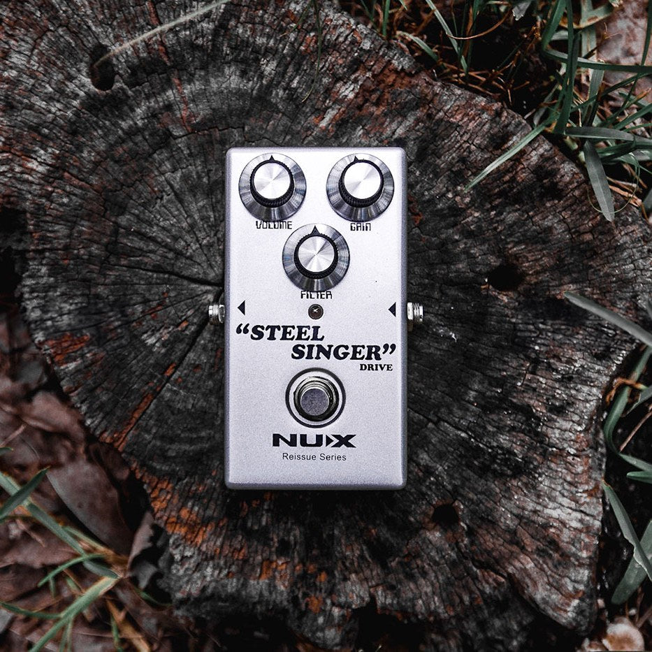NU-X Steel Singer analog drive guitar pedal in silver with Volume, Gain and Filter knobs and foot switch, shown on a weathered tree stump.