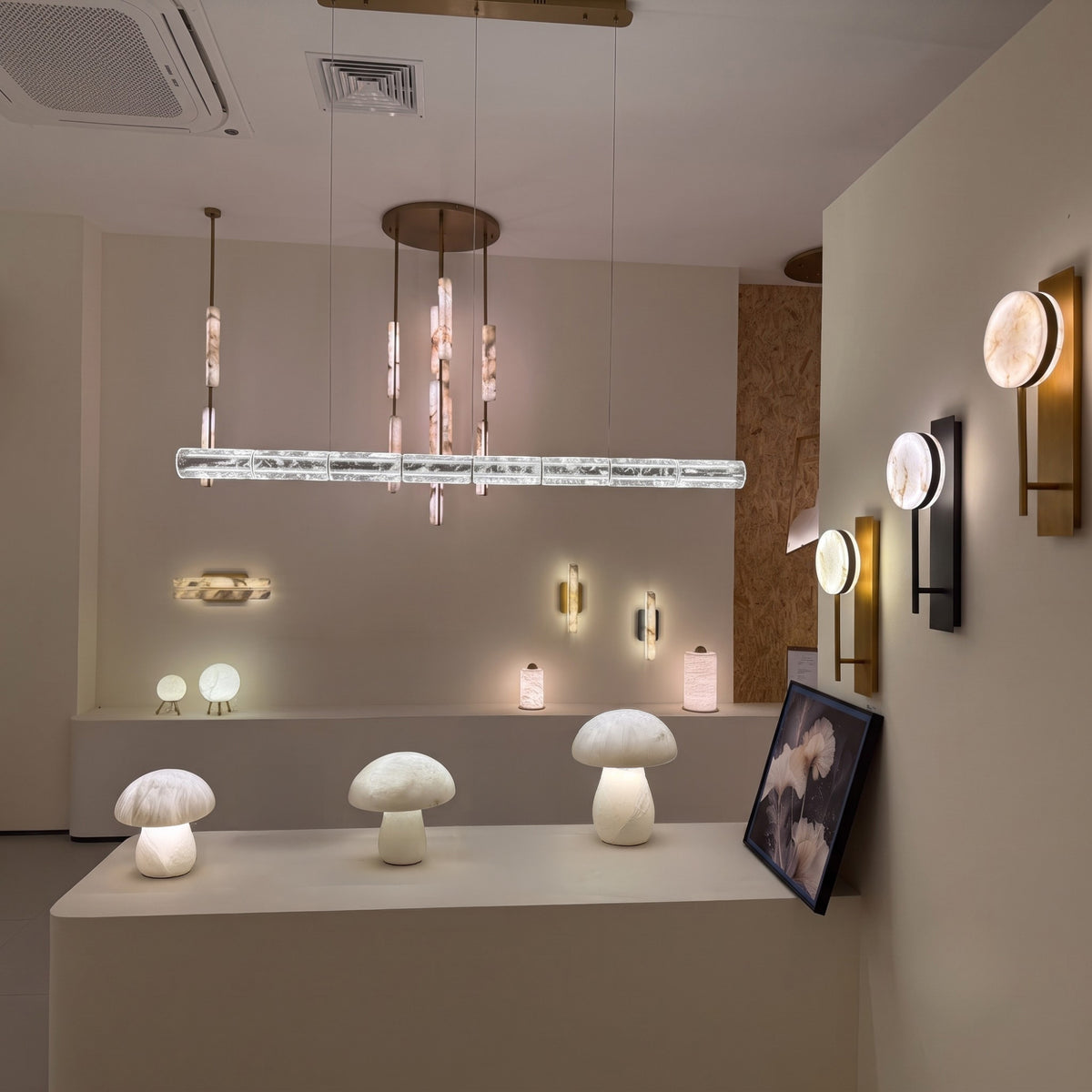 Liora LED Crystal Linear Chandelier 1.6m in chrome, shown as a segmented crystal tube pendant on suspension cables, illuminated in a showroom with mushroom lamps and wall lights.