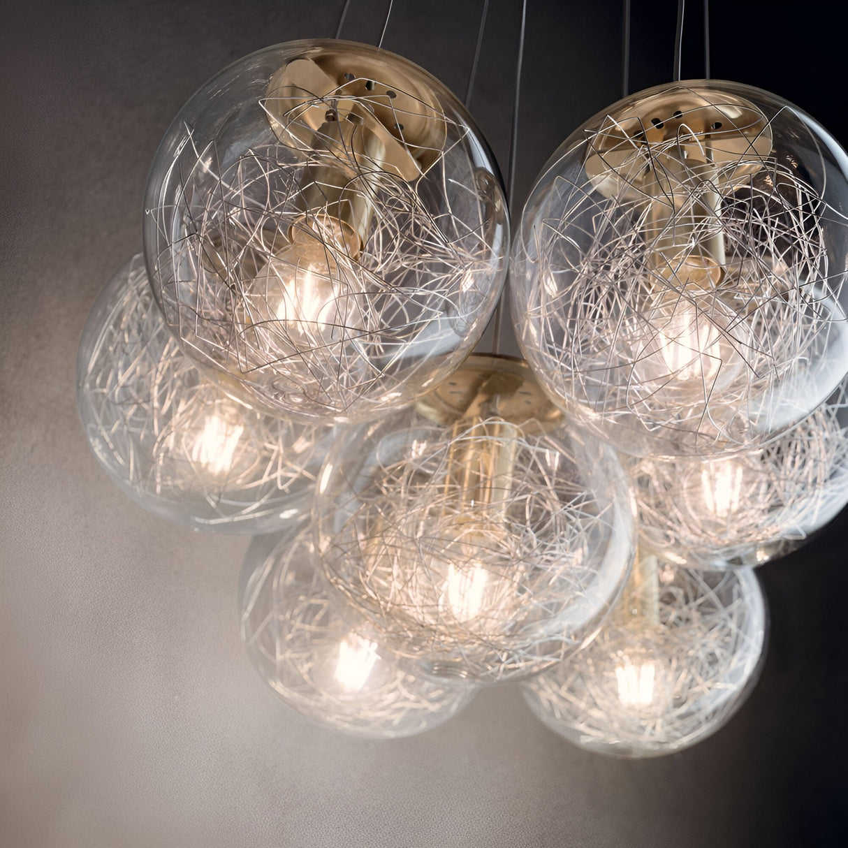 A group of Lyria 7 Light Cluster Pendant lights with elegant round glass shades and a brass finish showcases an intricate wire network, emitting a warm glow. These modern design pendants hang from the ceiling, offering a sleek and contemporary lighting fixture.