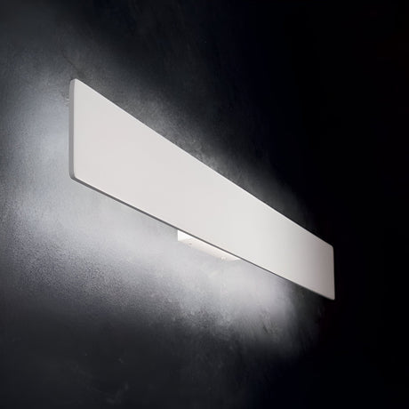 The Flara LED Wall Light 12.5W 3000K in White, measuring 29cm, casts a soft white light against a dark wall, creating an energy-efficient gradient effect with its sleek, modern rectangular design.