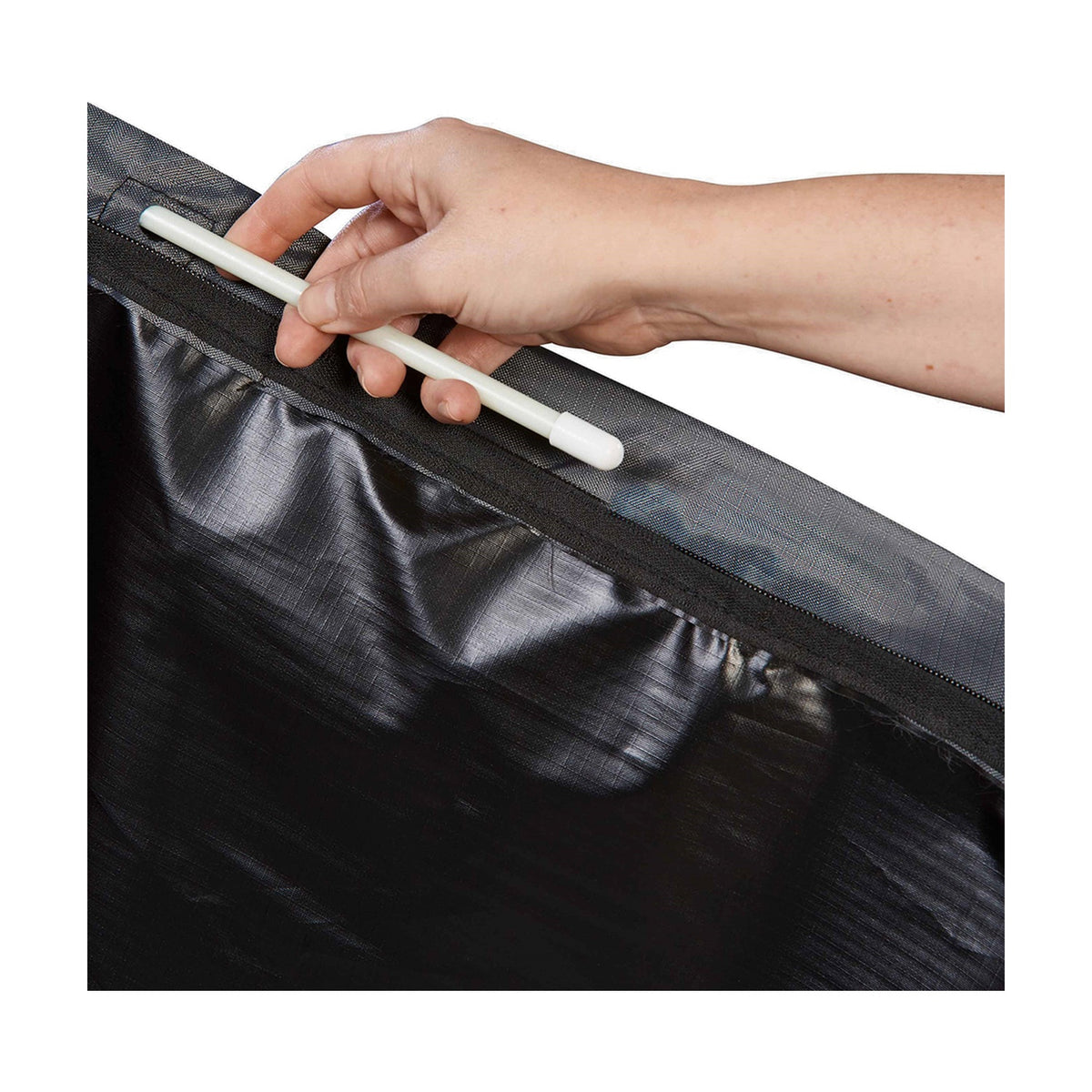 A hand inserts a white support rod into the zipped opening of the Parasol Aerocover, revealing its anthracite fabric lining and stitched seam detail.