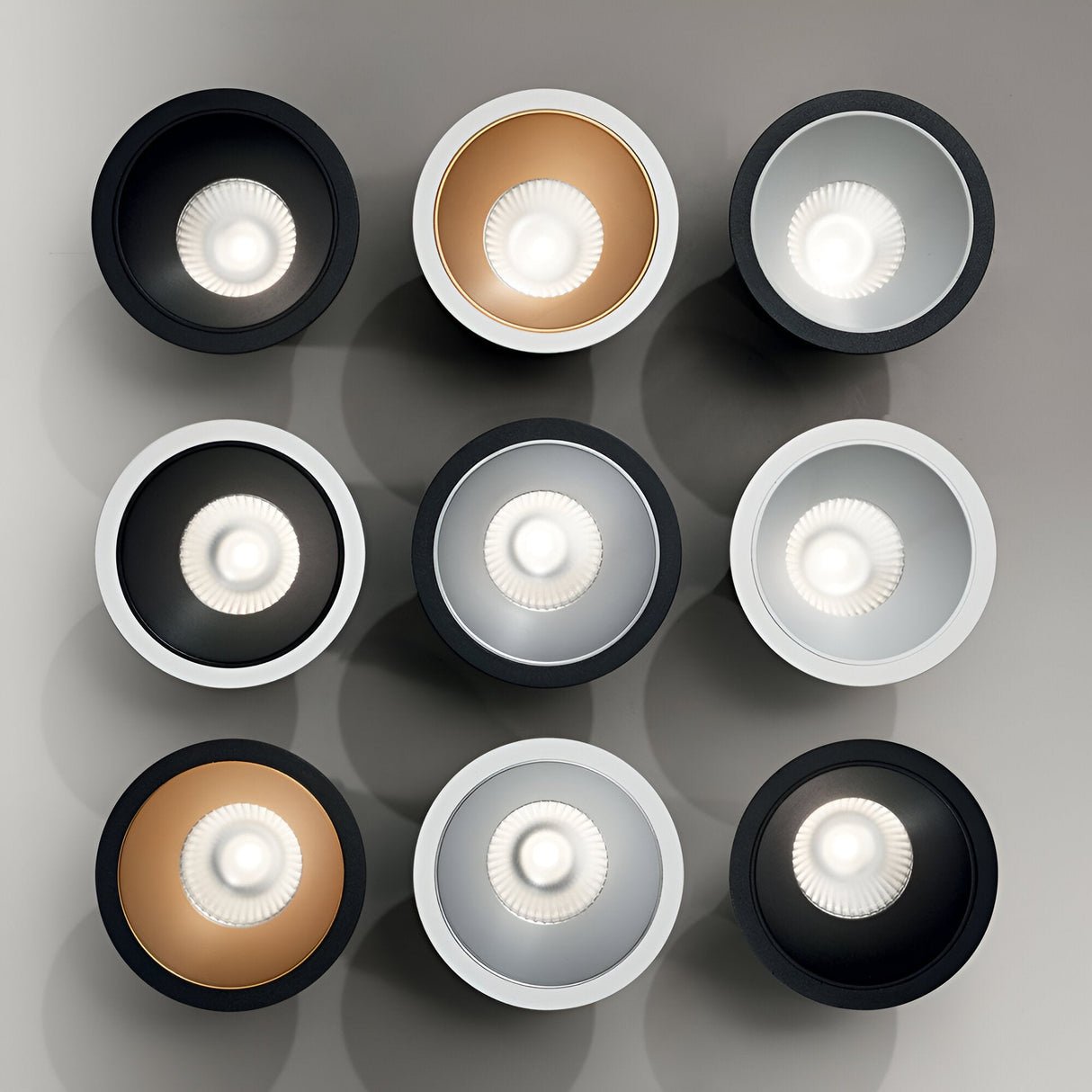 A 3x3 grid of the Sally LED Round Recessed Trim Downlights, each featuring black and white trim, emits a soft 3000K light. This illuminated arrangement against a plain background creates a modern and geometric aesthetic.