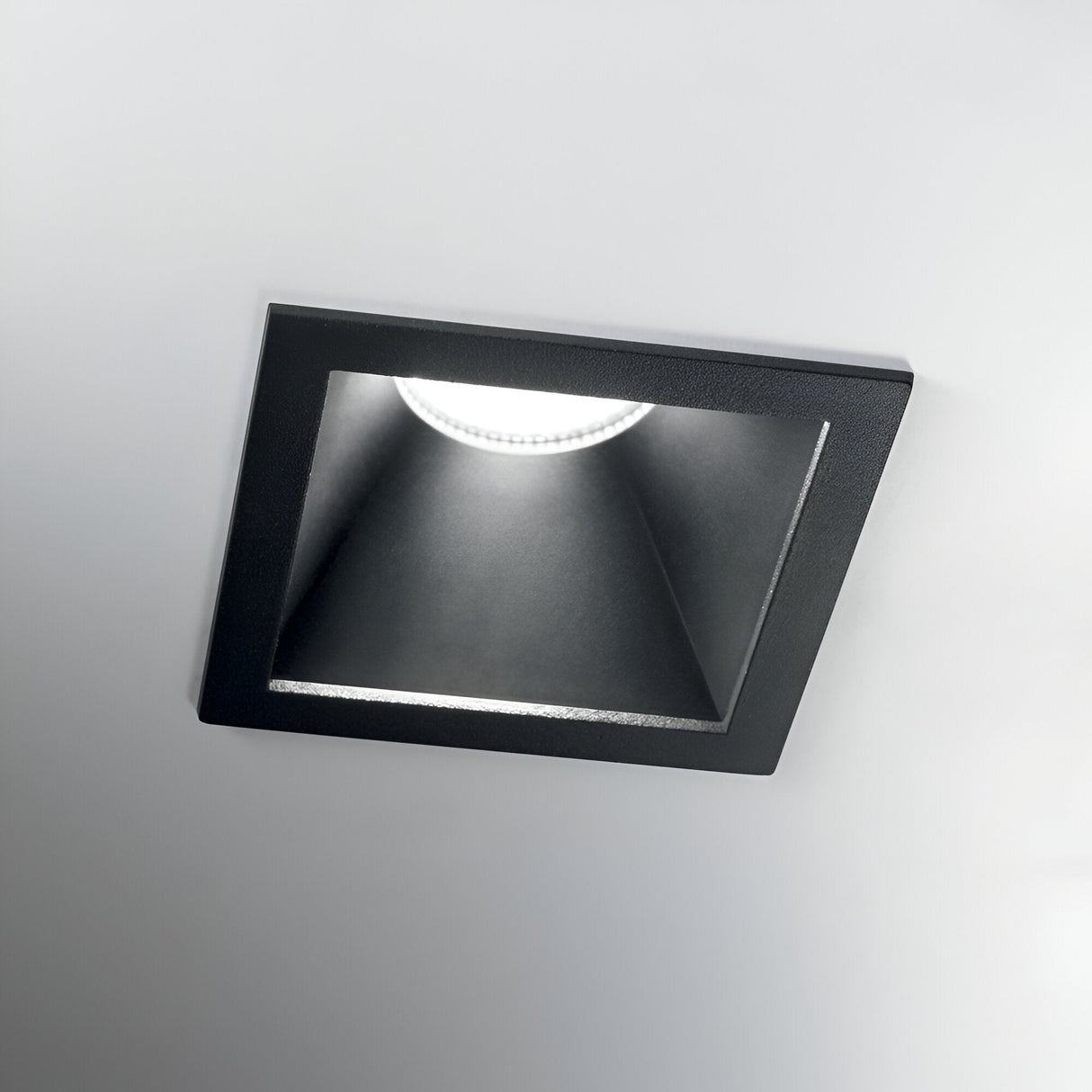 The Sally LED Square Recessed Trim Downlight, with a black frame and energy-efficient LED technology, is mounted in the white ceiling. It emits a soft, focused light downward at 11W with a color temperature of 3000K.