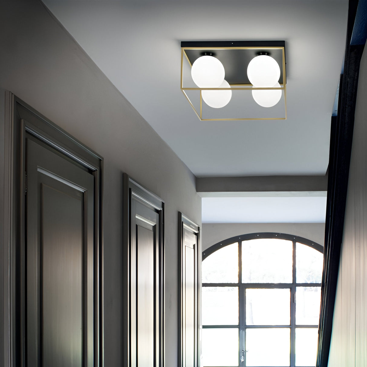 A modern hallway with dark paneled walls and a window at the end features the Dawn 4 Light Flush - Brass on the ceiling, showcasing a square design with four round white bulbs, epitomizing contemporary elegance.