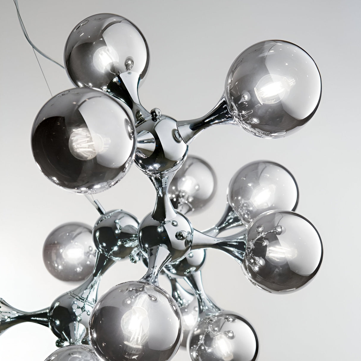 Close-up of the Emblaze 15 Light Suspension - Silver chandelier featuring spherical, metallic fixtures arranged in an abstract, molecular style against a light gray backdrop, highlighting its modern elegance and versatile ambiance with dimmable lighting.