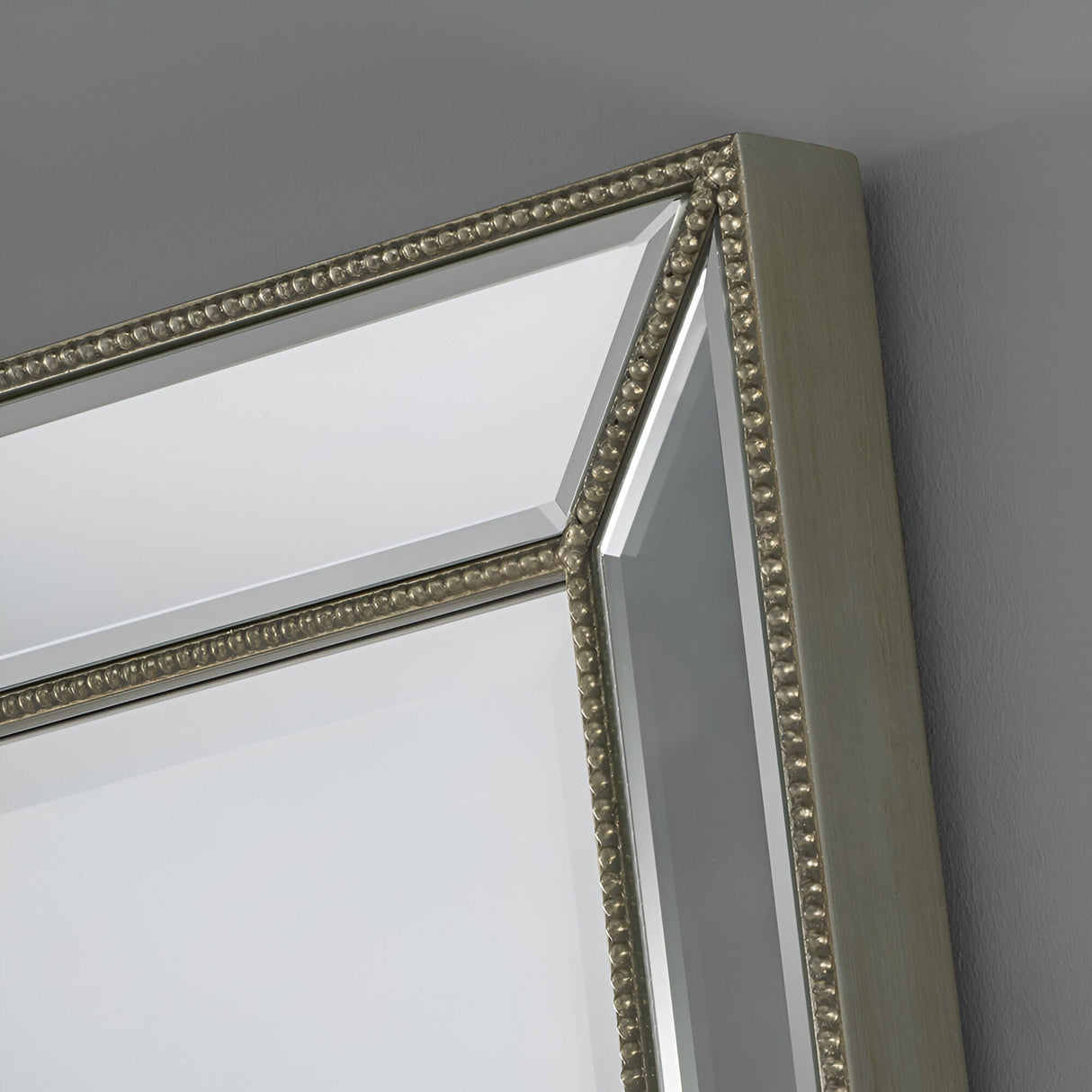 Close-up of the Celestia Rectangular Wall Mirror in Champagne Gold (91 x 61cm) featuring a decorative metallic beaded frame and beveled edges, mounted on a gray wall with its reflective surface visible.