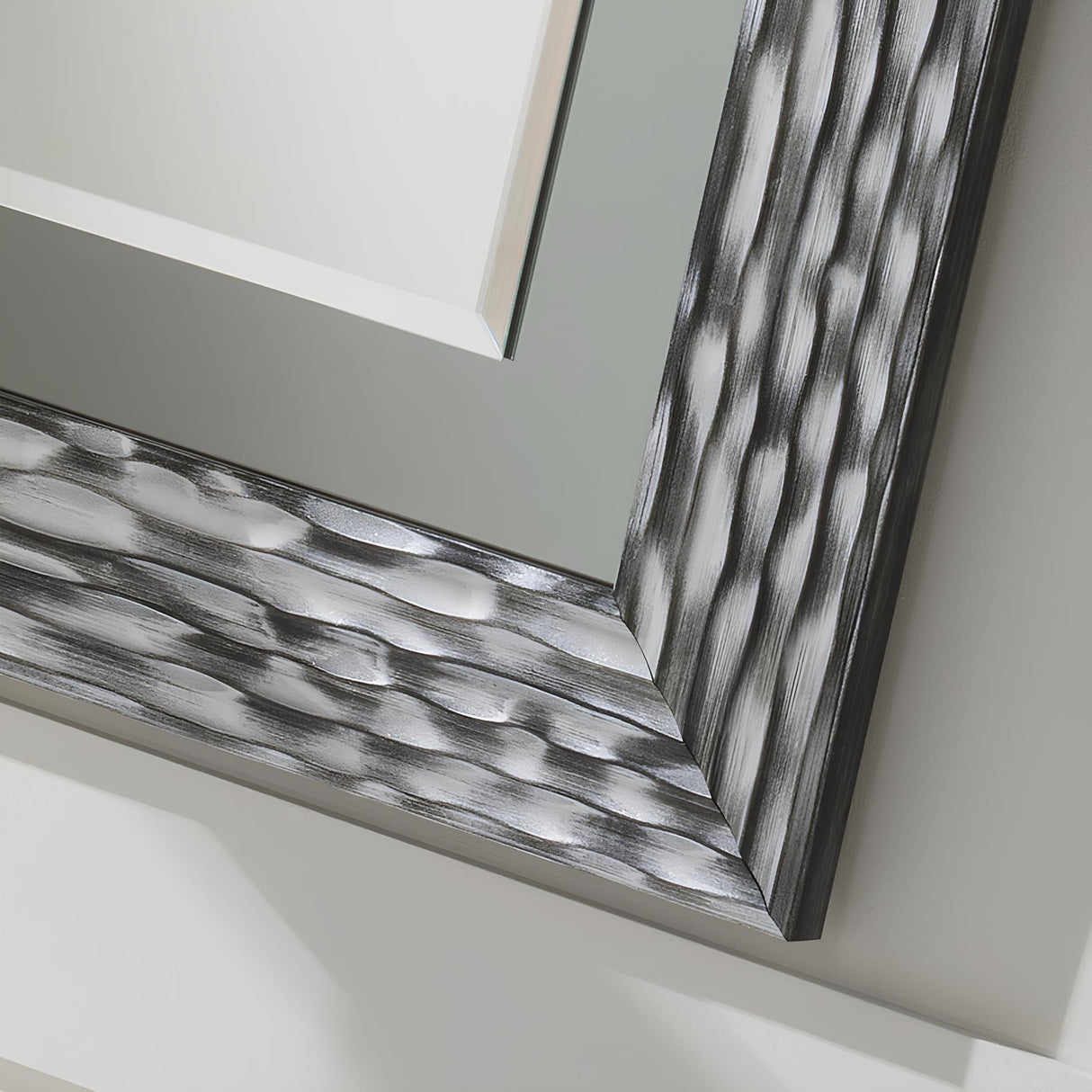 Close-up of the textured, dual-tone frame corner of the Halo Rectangle Wall Mirror - Black/Silver Lacquered, featuring a wavy, metallic finish and reflective surface. Mounted on a light wall, it casts shadows that enhance its three-dimensional aspect.