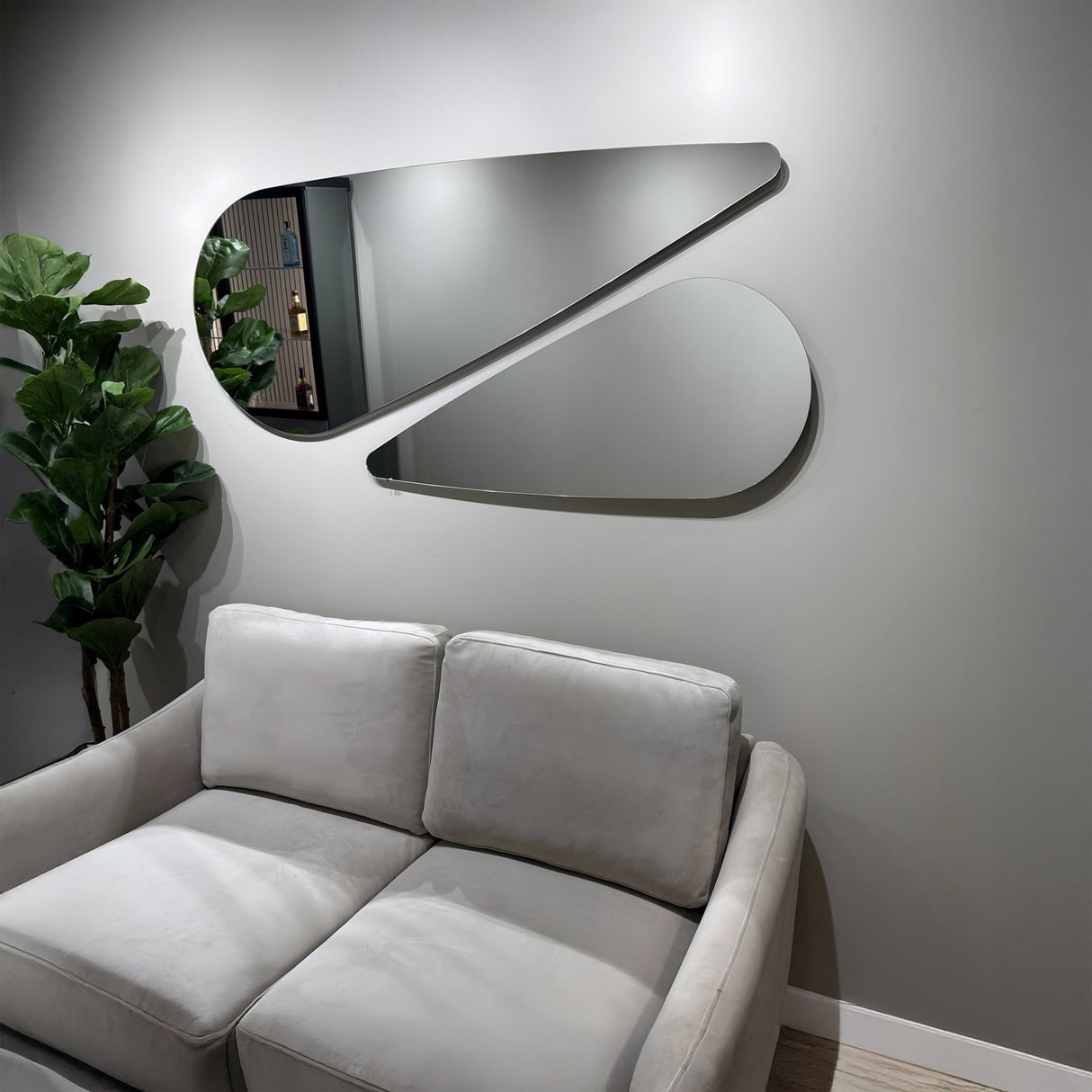 A modern living room with a light gray sofa, a tall green plant, and two Oculus Droplet Wall Mirror - Clear pieces with a frameless design on a gray wall, creating a stylish and minimalistic look.