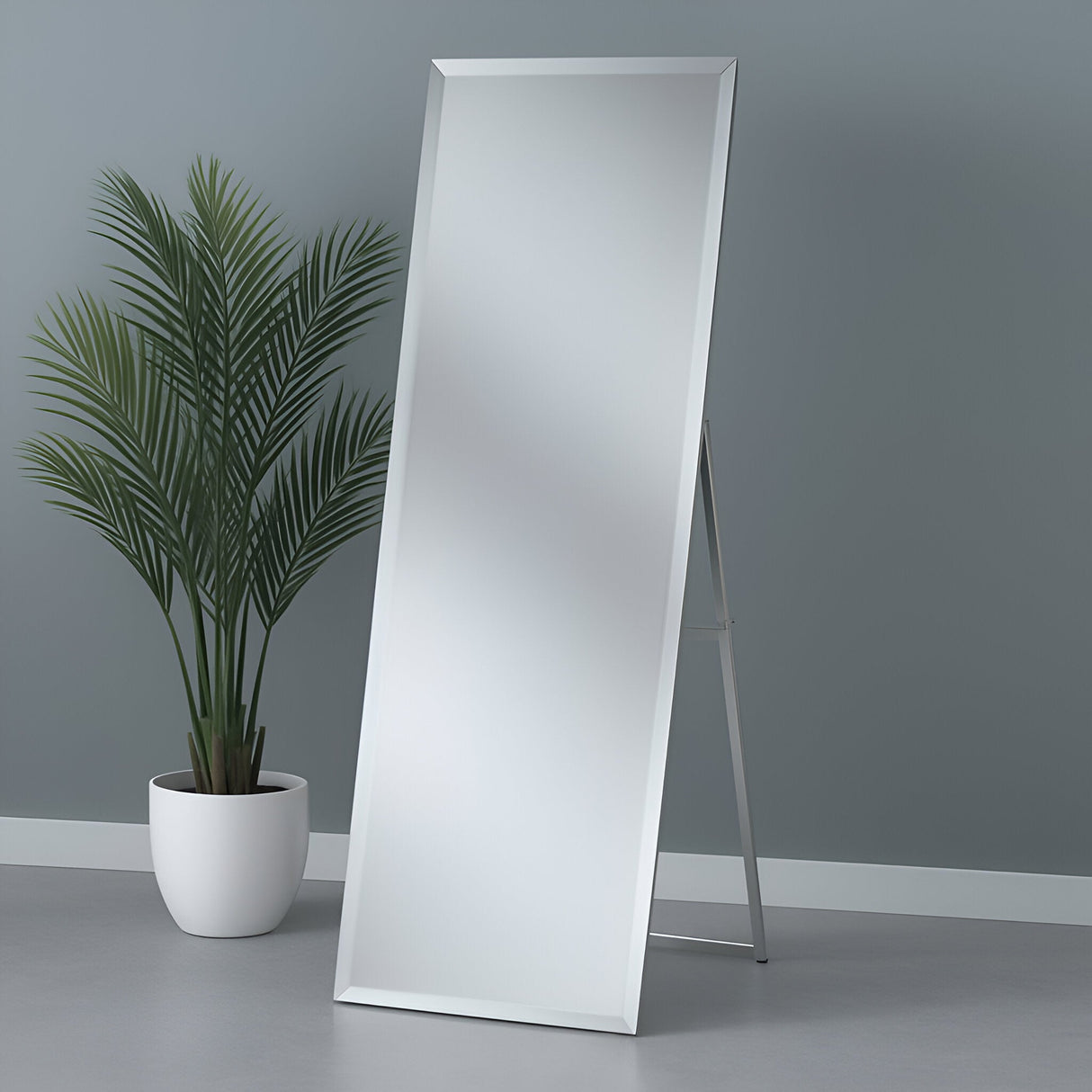 The Nimbus Free Standing Mirror Silver (153x47x42cm) stands on a light gray floor beside a potted green plant against a plain gray wall.