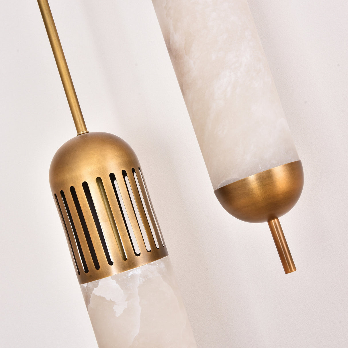 Close-up of the Zerith LED alabaster tube pendant light, showing natural alabaster cylinders with fluted brushed brass collars and domed brass end caps against a plain white background.