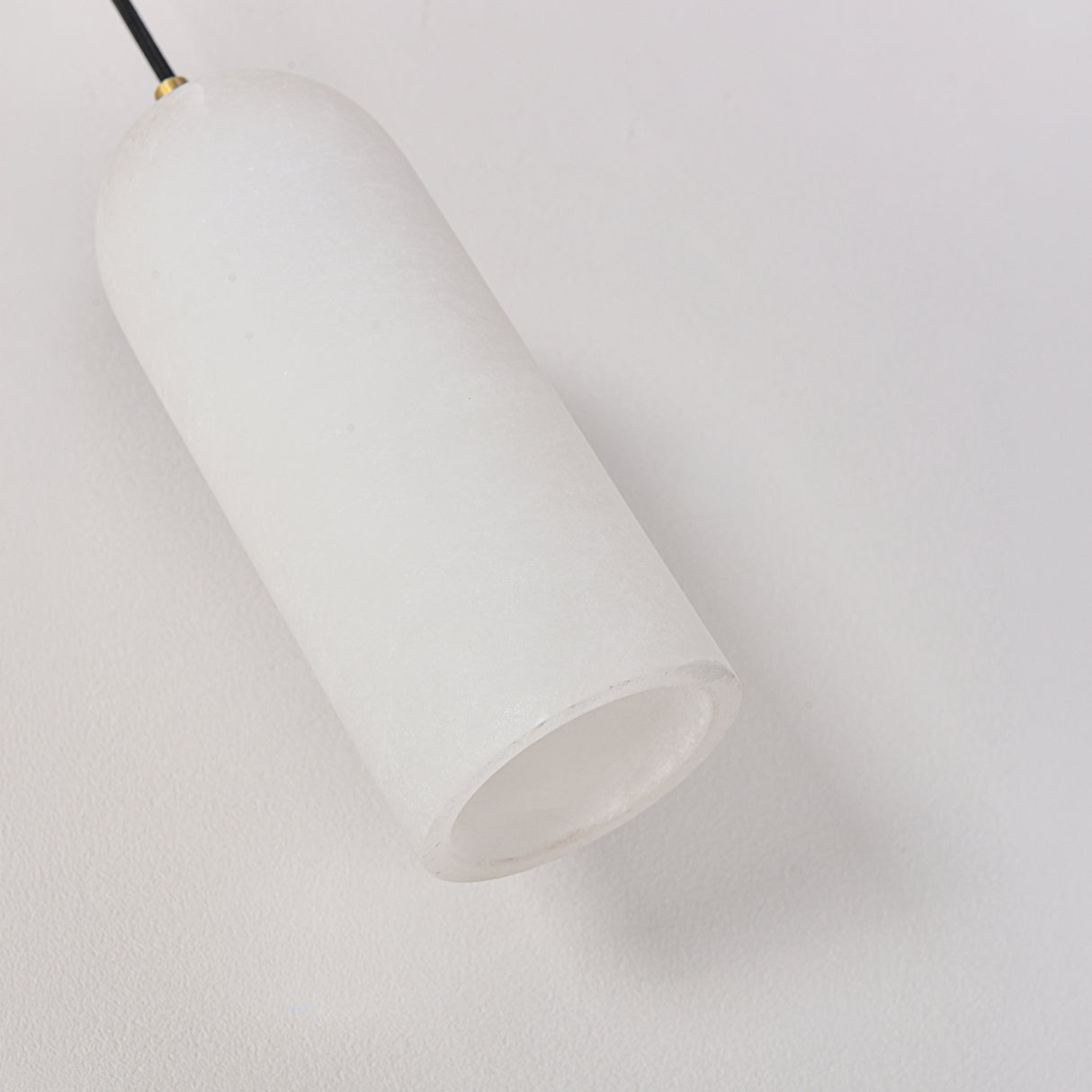 Velmora slim cylindrical alabaster pendant light in soft white, with brass ceiling plate and black flex, shown close-up against a plain background.