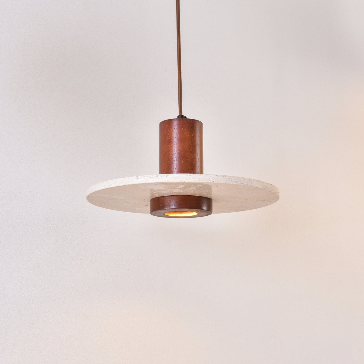 Torvane 1 Light Travertine Disc Pendant Light with a light beige stone disc and walnut brown wooden column, glowing centre light, on a plain white background.
