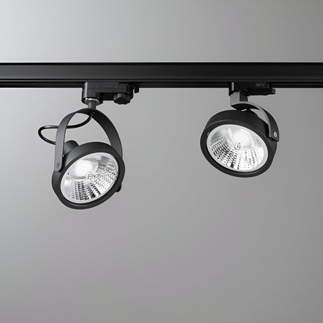 Two Glim Three Phase Track Spotlights in black are mounted on a black rail against a gray background. These lights boast a sleek, industrial design with circular heads and adjustable angles, complete with an adjustable diffuser for customized and focused illumination.