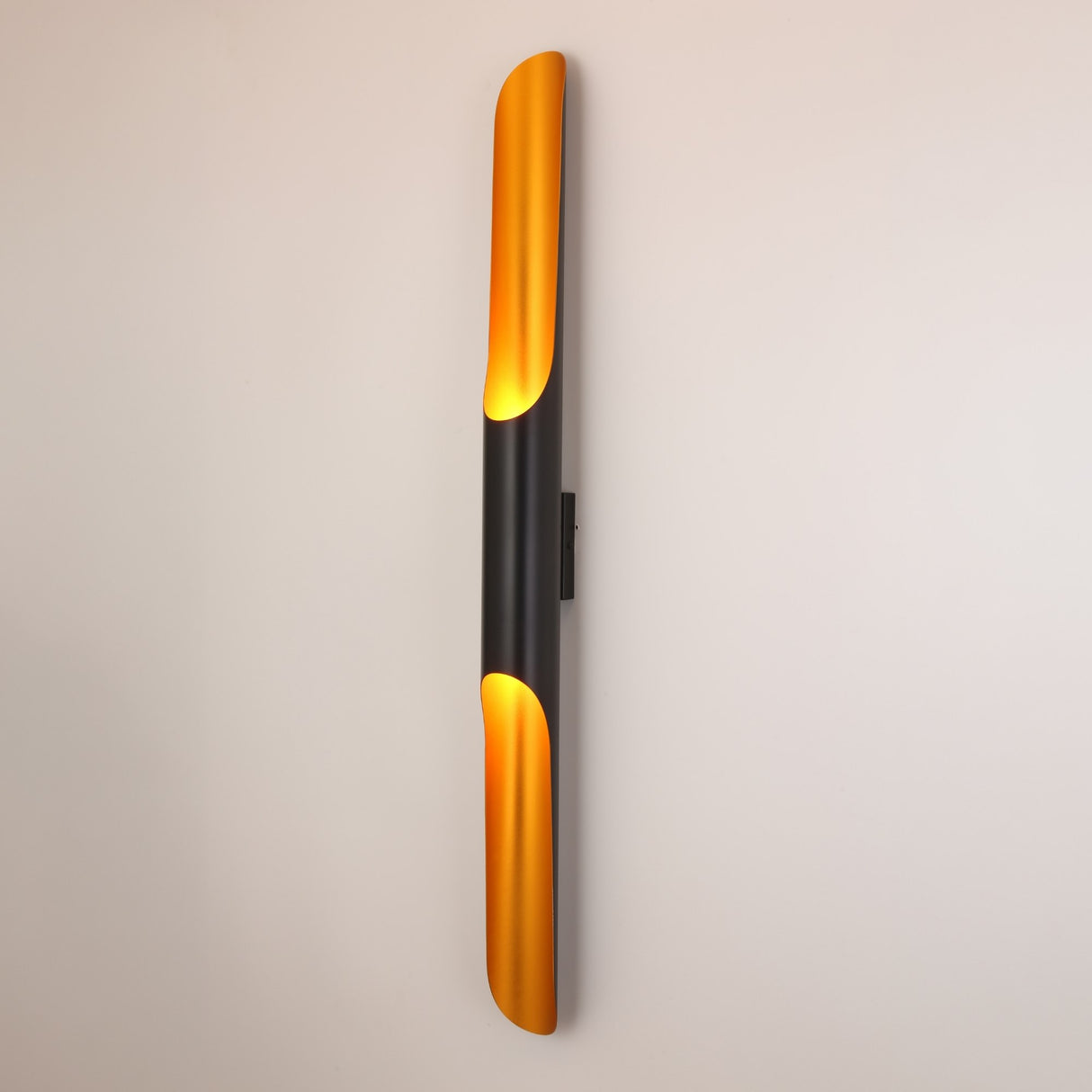 The Stealth 2 Light Wall Light in Brass & Black features a sleek vertical design with brass accents, casting warm light against a plain white wall.