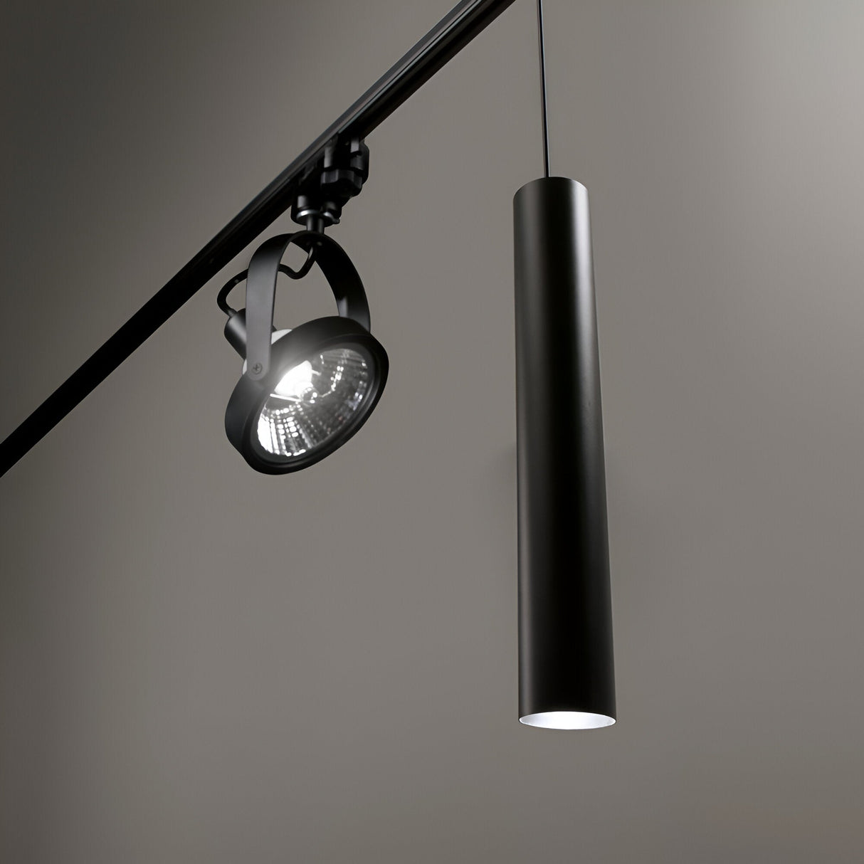 The Noctis 1 Light Track Pendant in matte black, measuring 6cm, is a modern fixture that combines a sleek track pendant light with an adjustable spotlight, mounted on a minimalist ceiling rail against a neutral gray background.