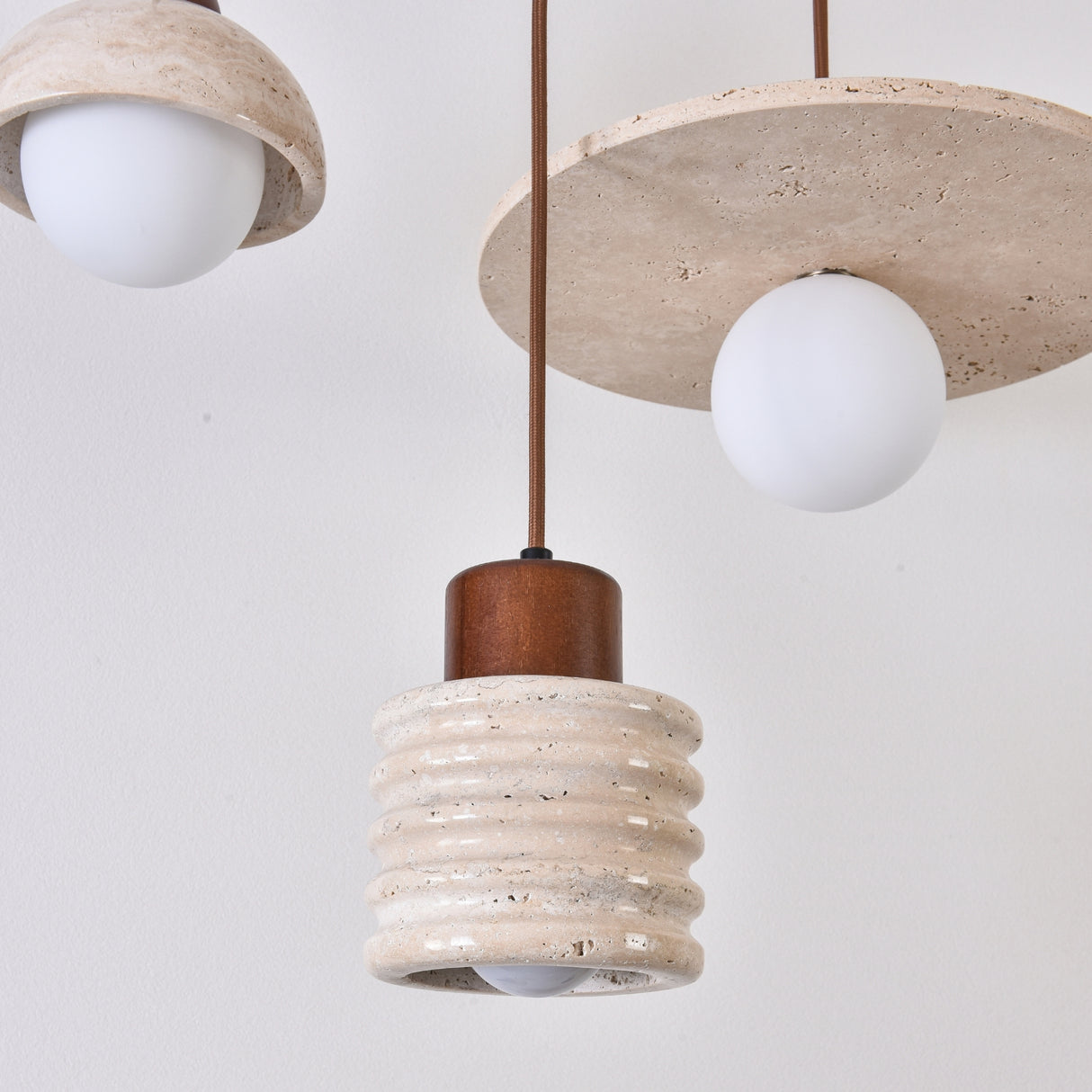 Rivano Ribbed Travertine Pendant Light with a ridged light beige stone drum, walnut wood top, and opal globe bulb, shown alongside matching disc-style pendants.