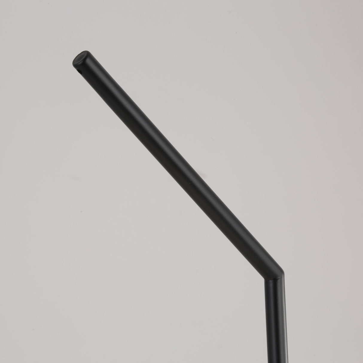 A black metal straw with a bent angle is displayed on a plain, light gray background beside the Vetra 1 Light Opal Glass Table Lamp in black.