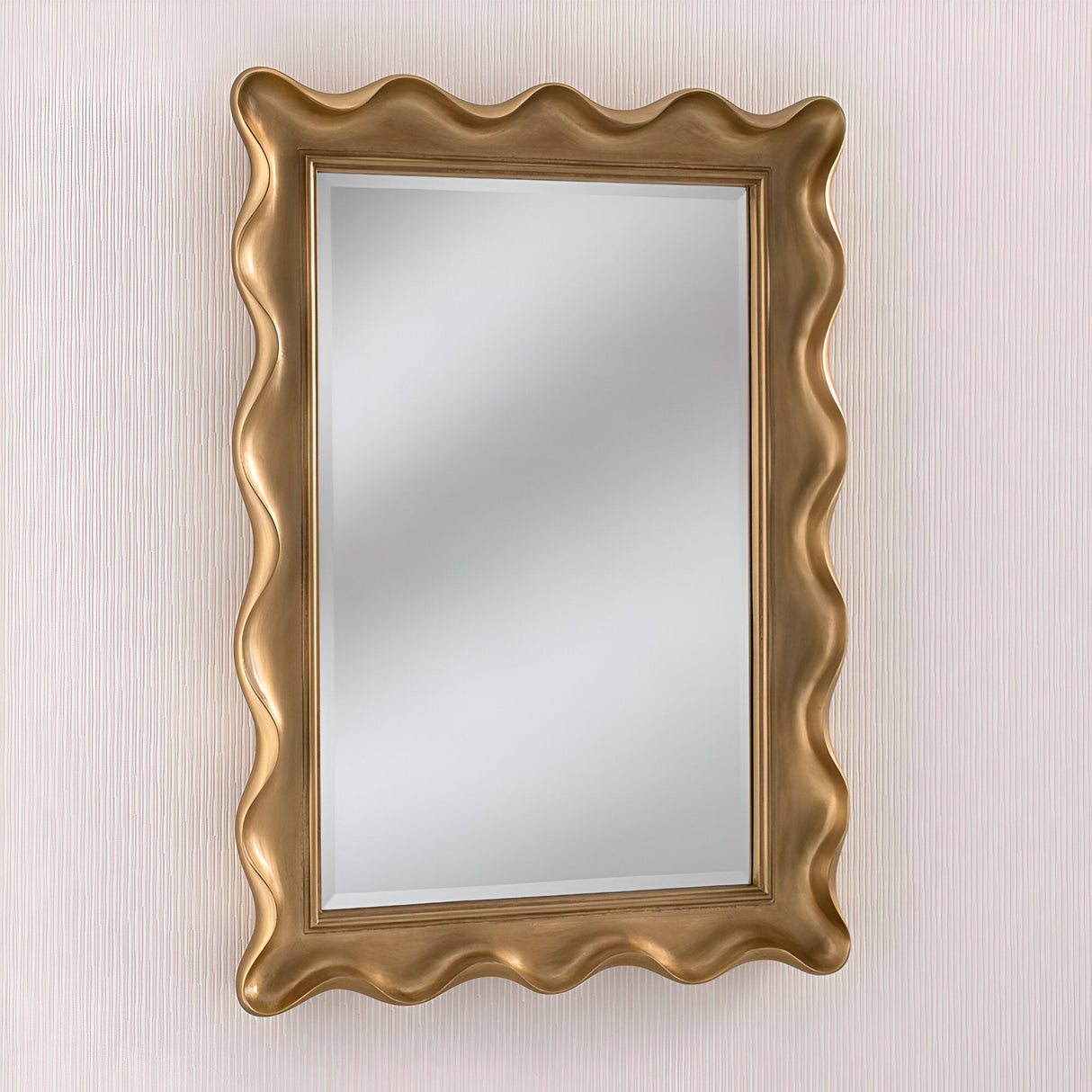 The Glaze Rectangle Wall Mirror Gold, measuring 113x83cm, features a wavy, gold-colored frame that brings vintage charm and serves as a decorative focal point against a light textured wall.