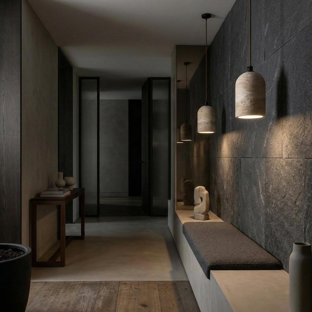 A modern hallway with dark slate walls, a minimalist bench, wood and stone accents, and the Belvora 1 Light Capsule Dome Travertine Pendant Light in light beige, plus vases and sculpture on a narrow table for a calm, sophisticated feel.