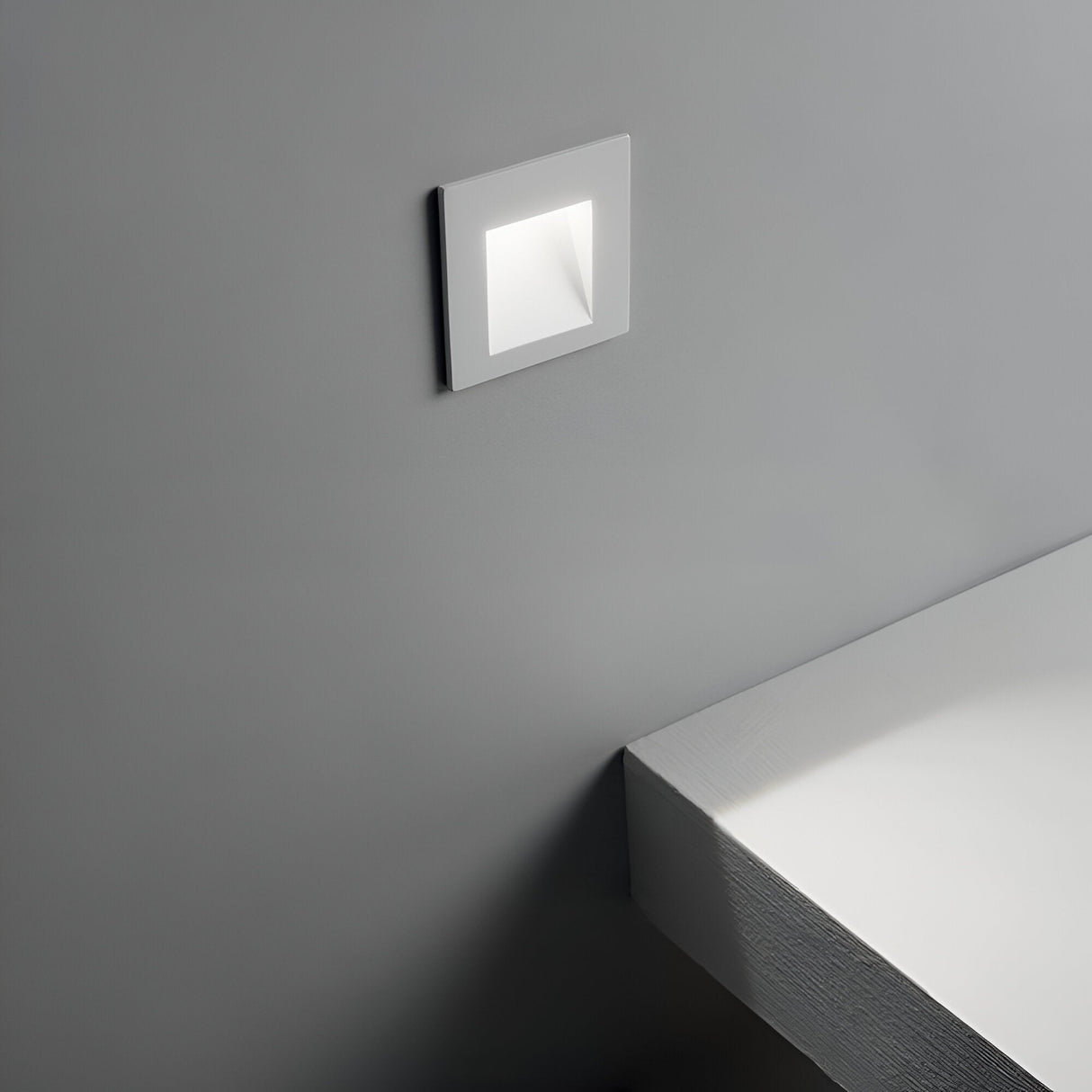 The sleek, contemporary design of a modern, minimalist interior is accentuated by the Pulse Outdoor LED Recessed Wall Light 2W 3000K in White. Its small, square form emits an energy-efficient brightness while the muted grey walls and adjacent surfaces enhance its outdoor LED aesthetic and weather-resistant properties.