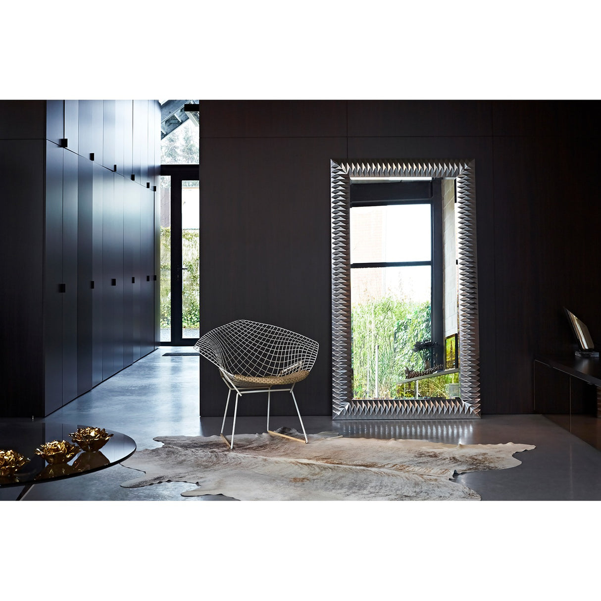 Nick Silver Leaf Full Length Mirror 189cm with faceted silver leaf frame, leaning against a dark wall beside a wire diamond chair in a modern hallway.