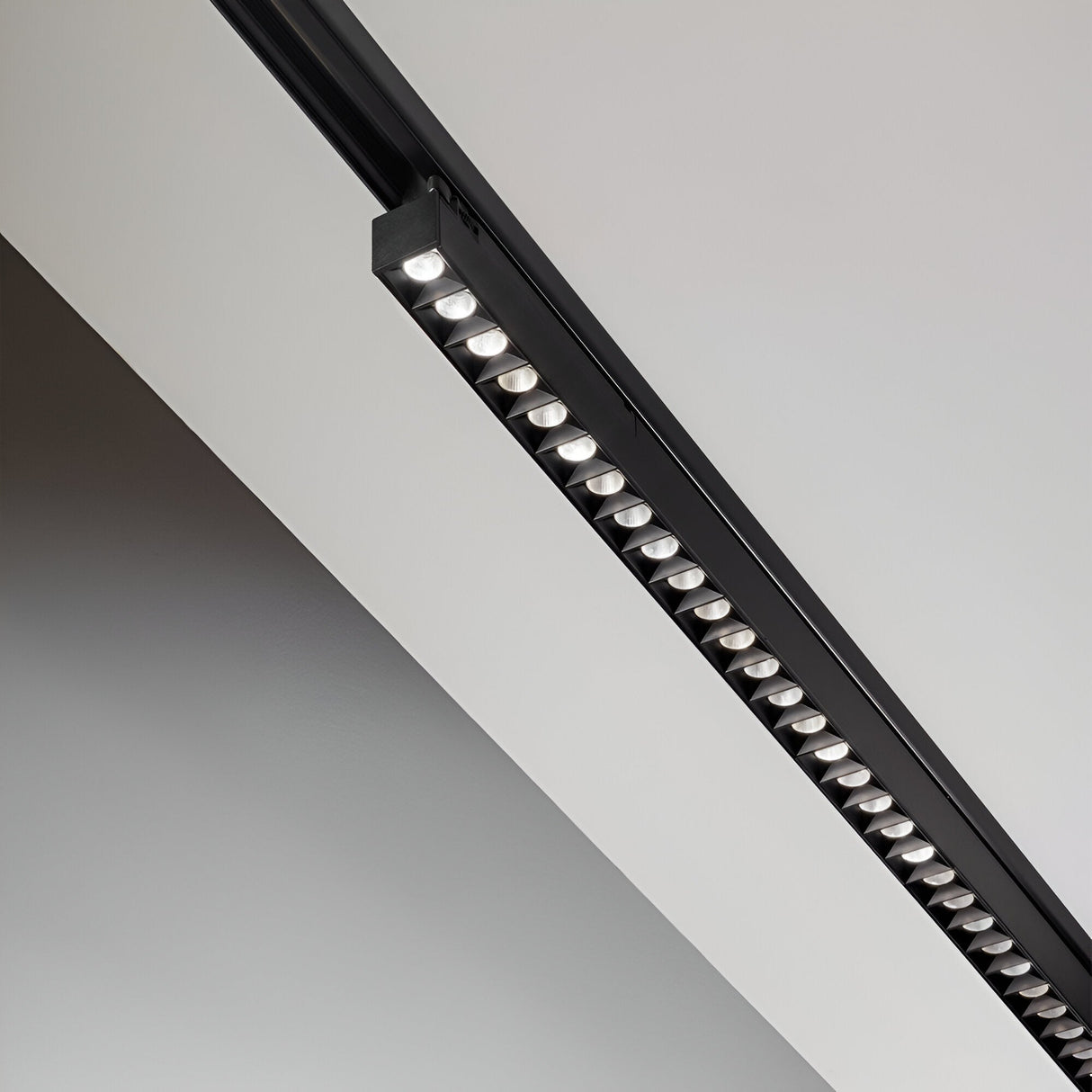 The Dune 3-Phase LED Linear Track Light 28W 3000K in black, measuring 1065mm, is mounted on a white ceiling. This sleek and energy-efficient fixture provides a minimalist and contemporary aesthetic with its modern geometric lines and multiple small bulbs that offer bright illumination.